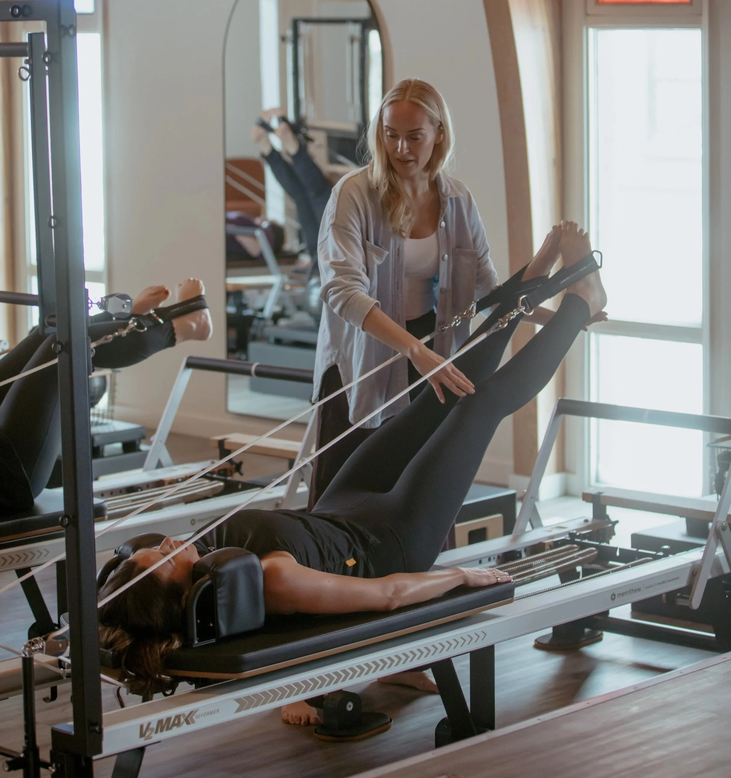 A woman receiving a Pilates session on a reformer machine from an instructor in a pilates studio.