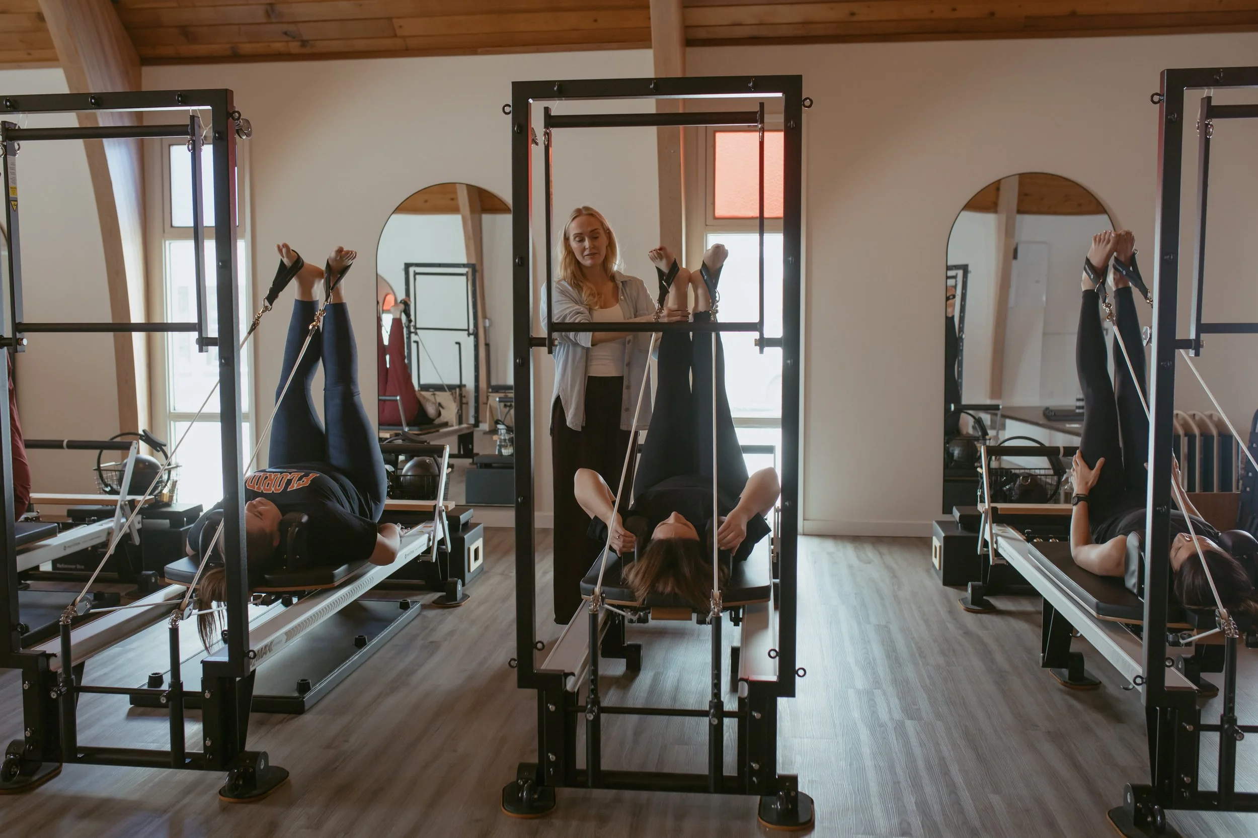 Instructor assisting clients with Pilates reformer exercises in a fitness studio.