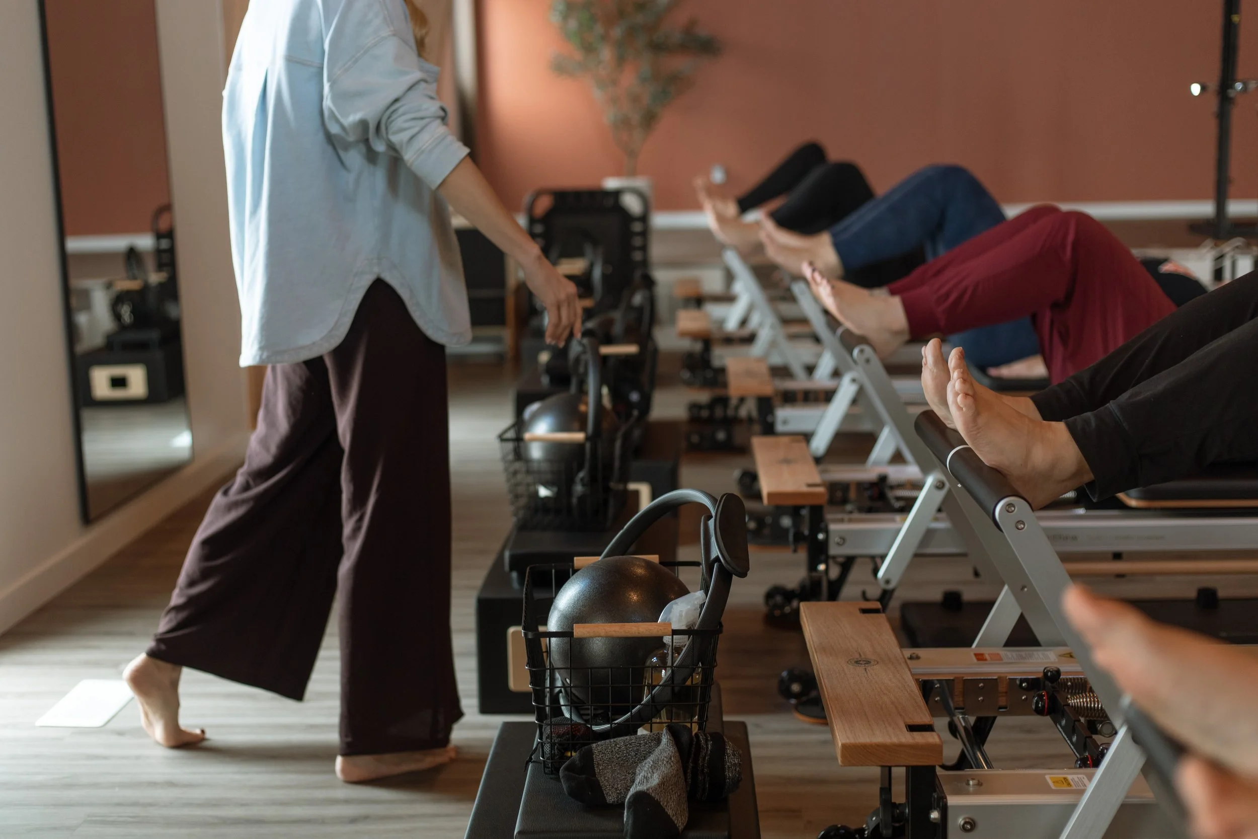 Instructor leading a seated fitness class with participants lying on reformers, lifting their legs and arms.