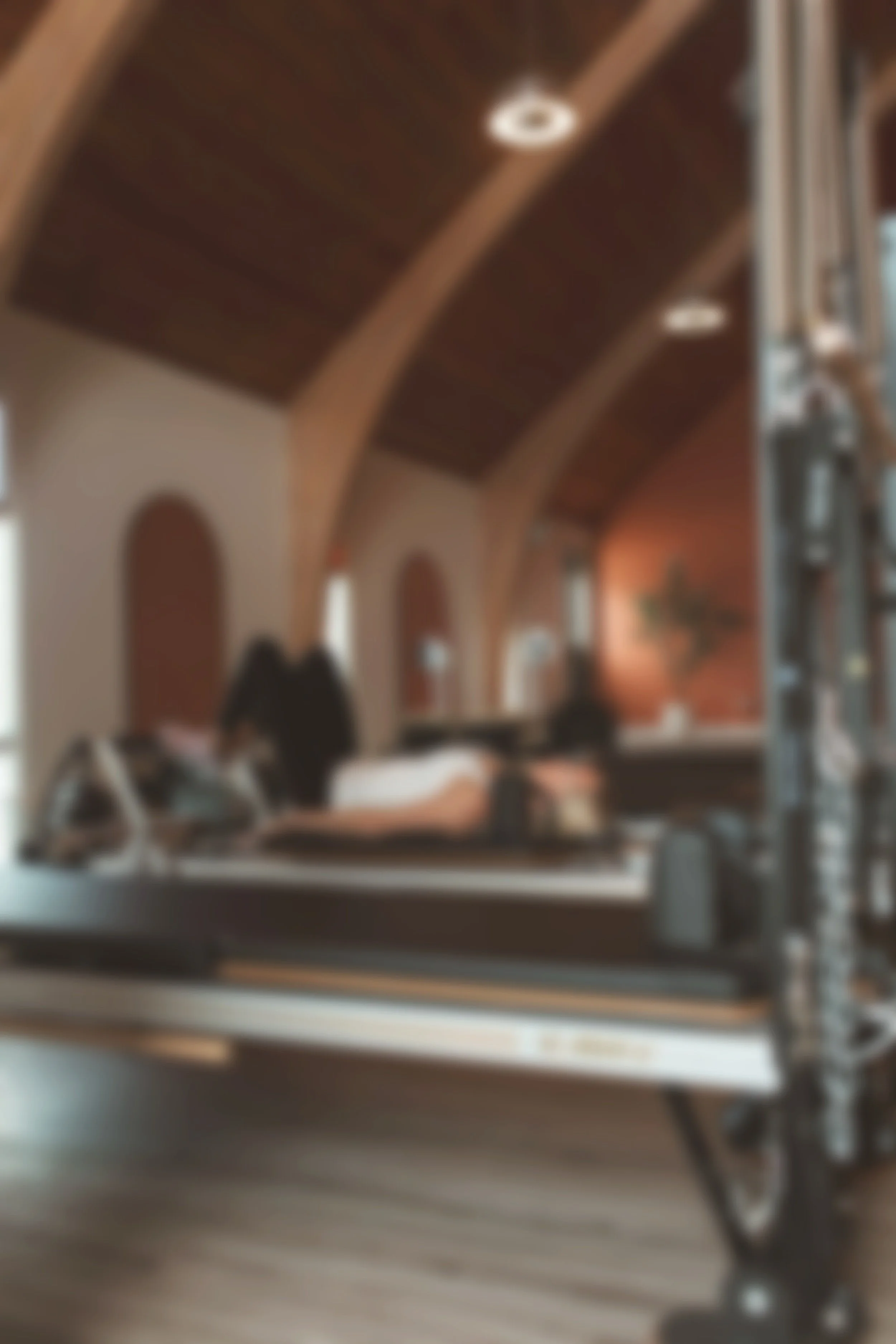 A blurred indoor scene of a pilates instructor demonstrating exercises on a reformer.