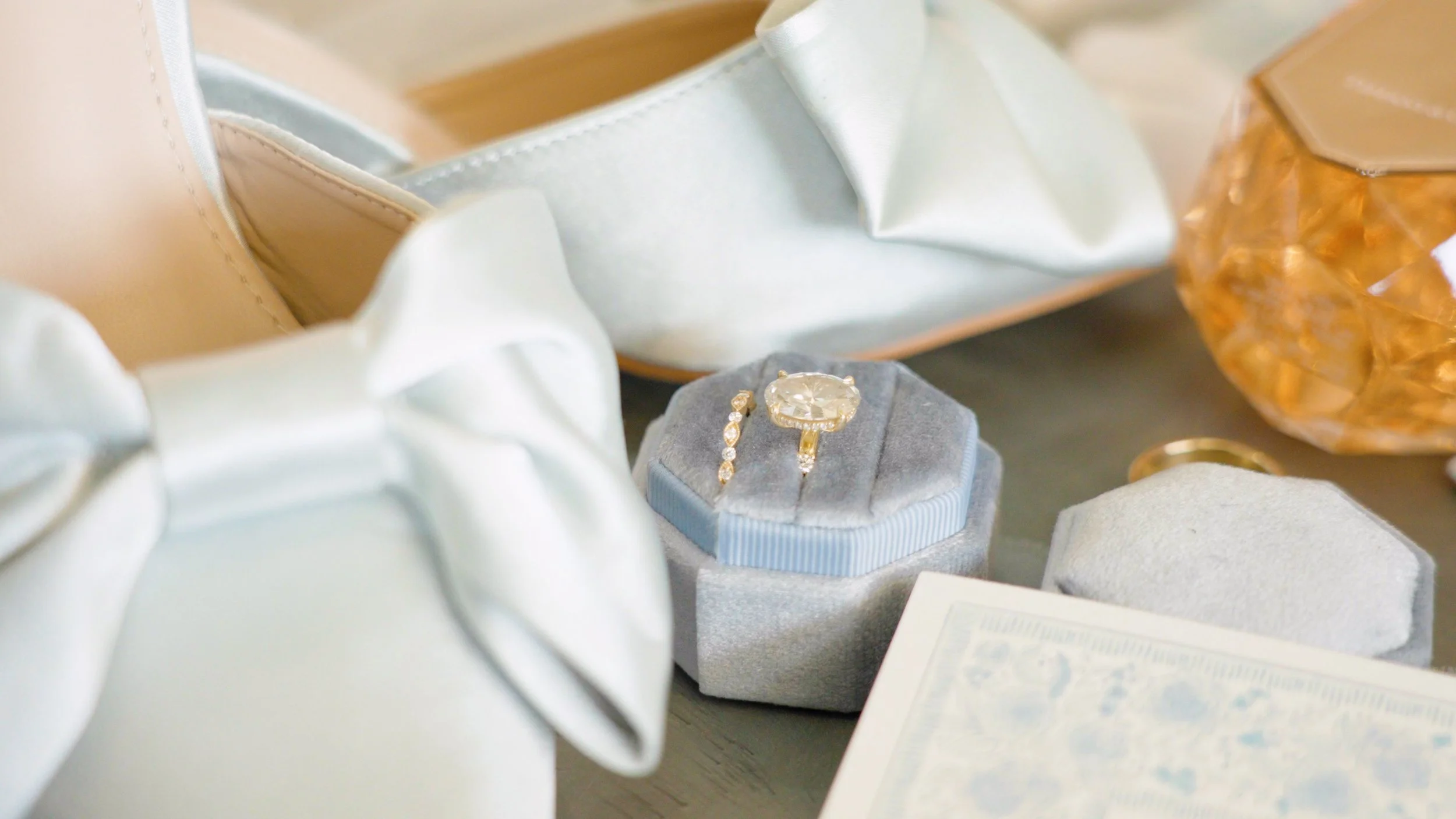 Close-up of a jewelry box with a gold ring and diamond bracelet inside, surrounded by satin fabric, a large amber-colored gemstone, and some papers.