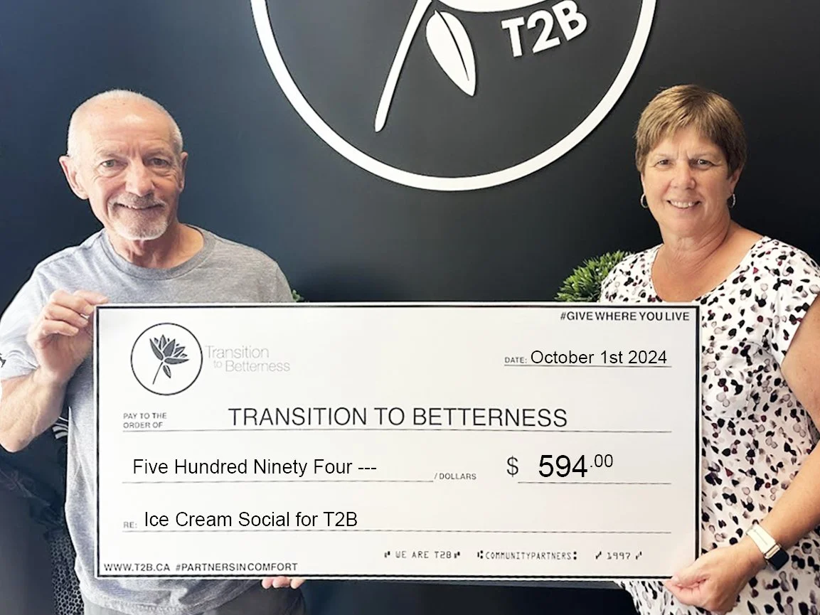 A man and a woman holding a large ceremonial check for $594, made out to 'Transition to Betterness' for an 'Ice Cream Social for T2B', dated October 1st, 2024, standing in front of a black wall with a logo that reads 'T2B' and a leaf design.
