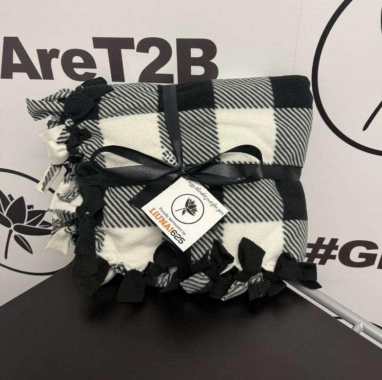 Three women standing in front of a sign that reads 'Zekelman' with the names 'Stephanie & Barry.' Each woman is holding a backpack, and the woman on the left is also holding a pink toy.