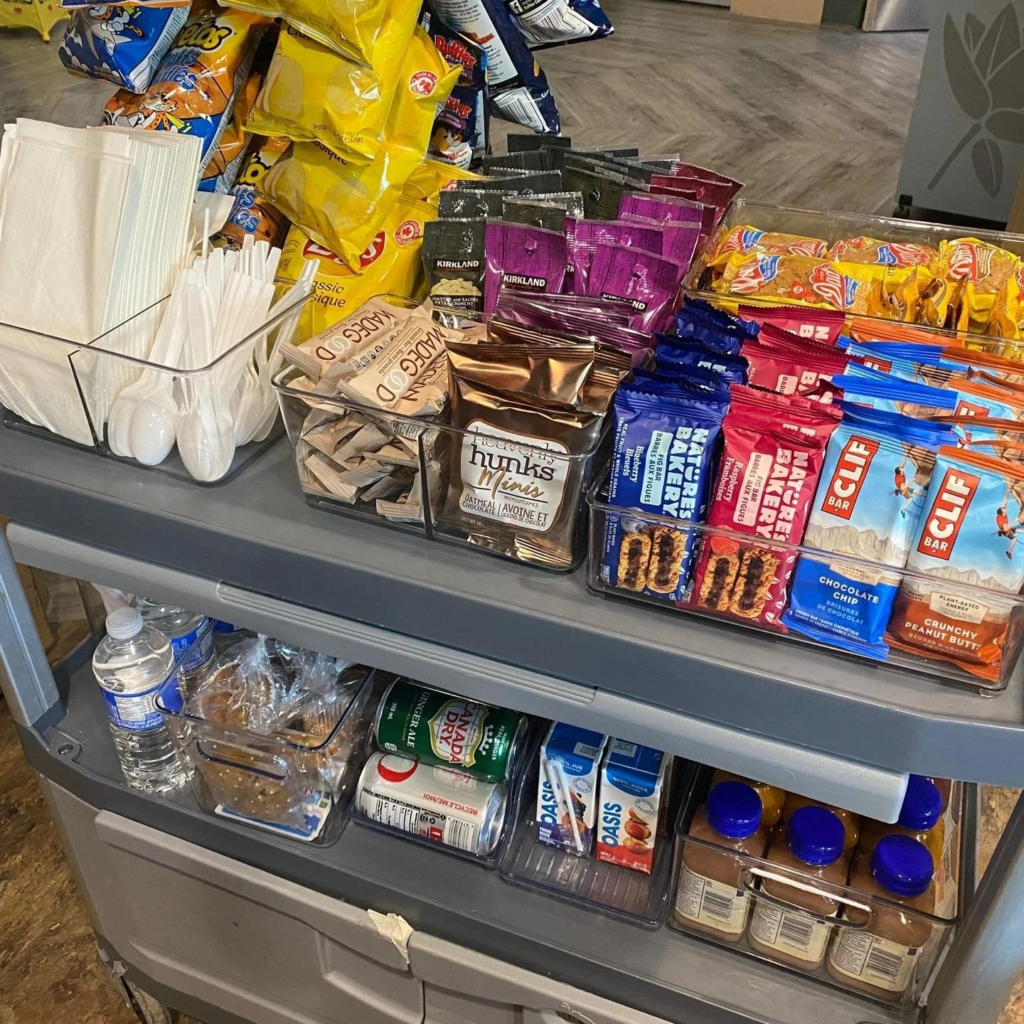 A snack cart with various chips, candy, drinks, and utensils, arranged in clear containers and on tiers.