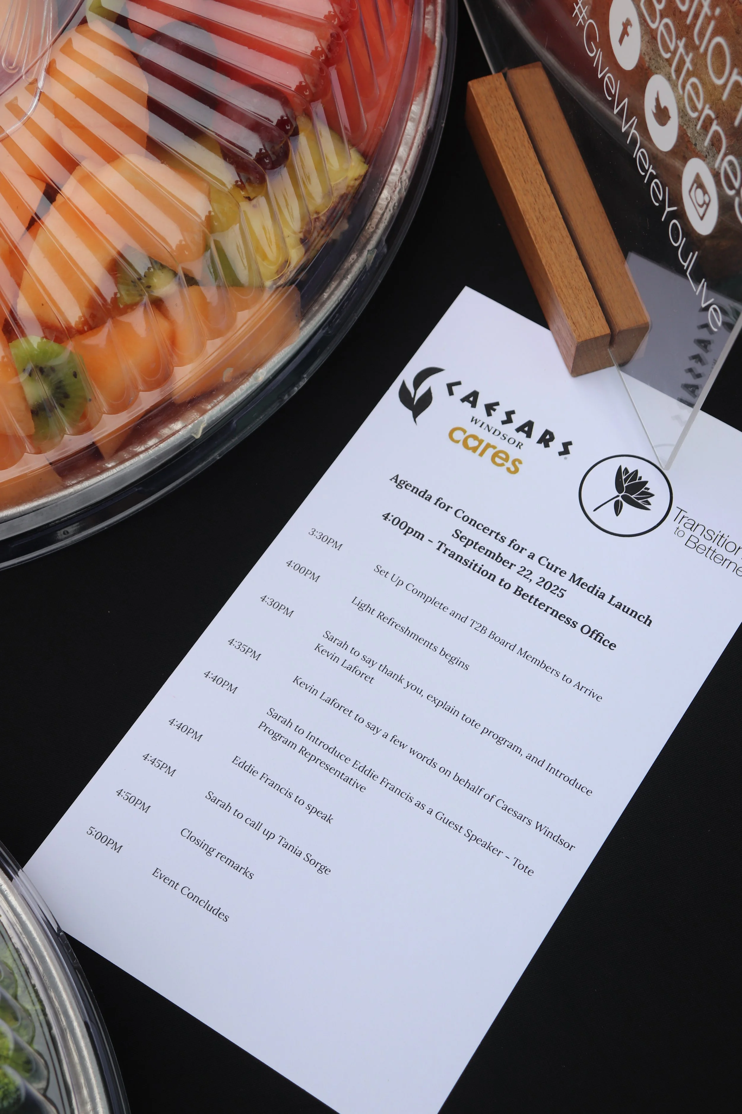 Agenda printed sheet for Caesars Windsor Cares event, outlining schedule from 3:30 PM to 5:00 PM on September 22, 2025, with a tray of assorted sliced fruits on a black table.