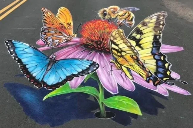Colorful chalk art of three butterflies and a bee on a pink flower with green leaves on a dark pavement
