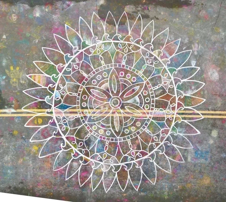 Colorful chalk drawing of a detailed geometric mandala design on a concrete surface.