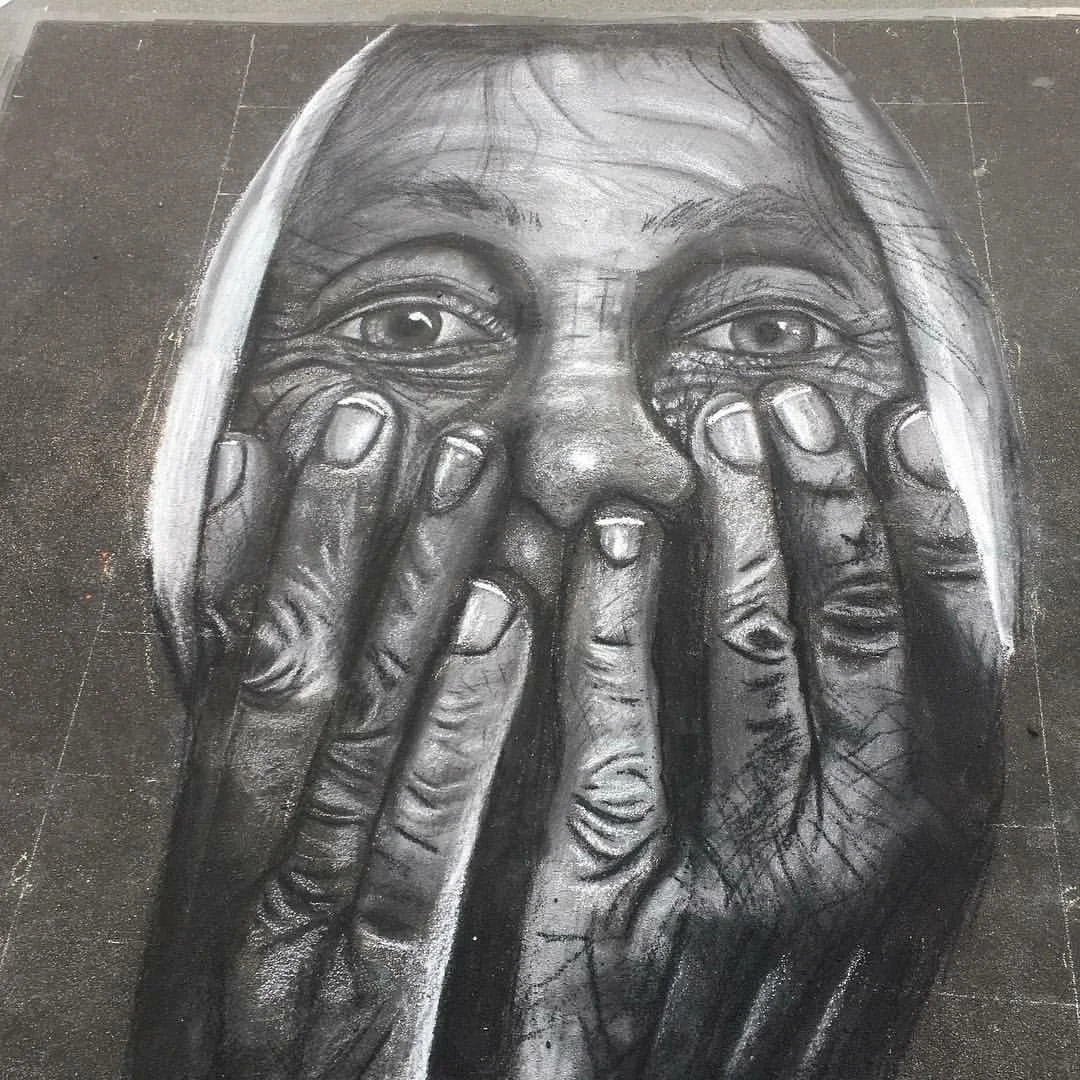 Black and white chalk drawing of a woman with hands covering her face, her eyes visible through her fingers, on a dark surface.