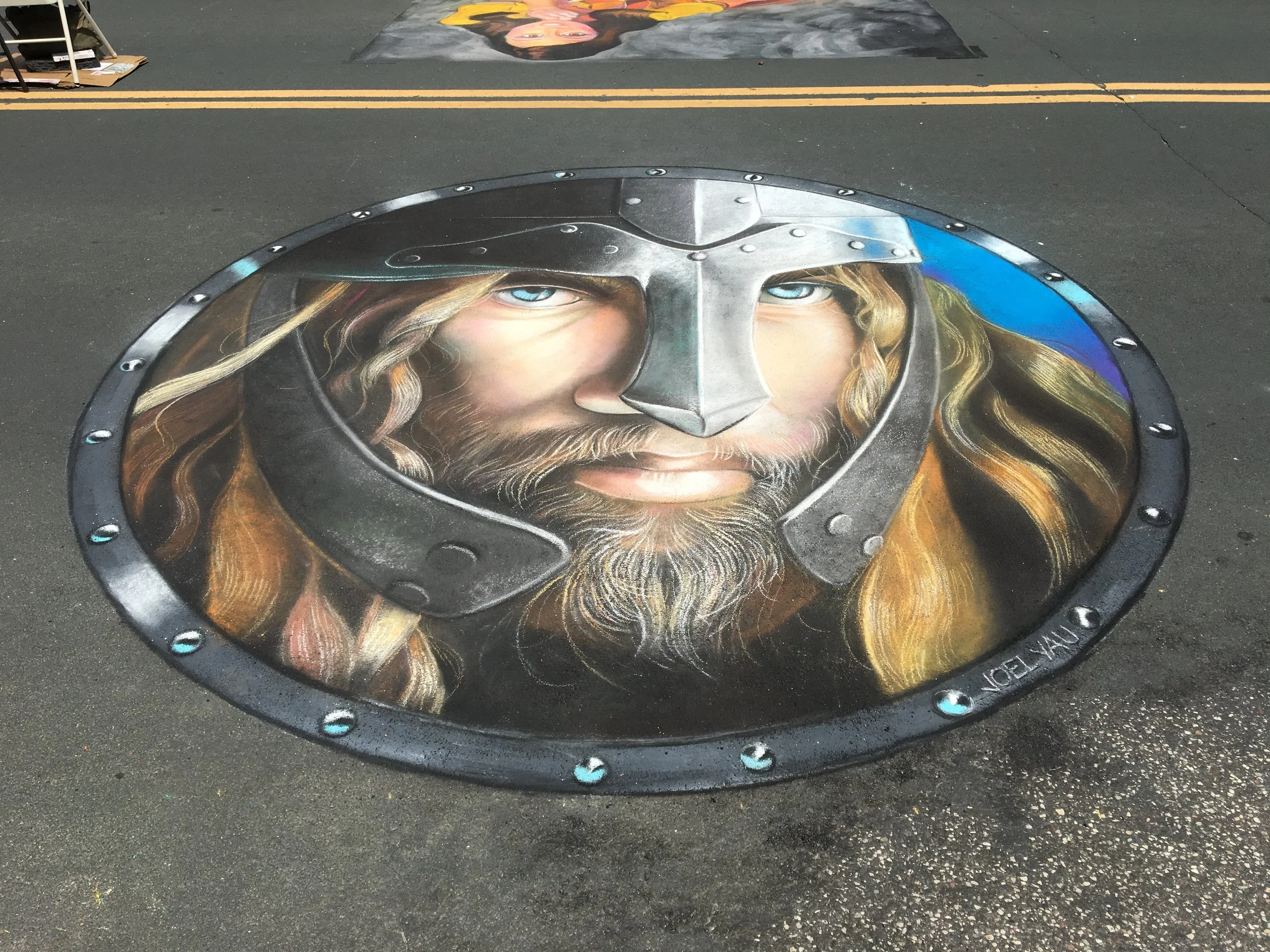 Street art painting of Thor with a helmet and long, flowing hair and beard, painted on a manhole cover on a street