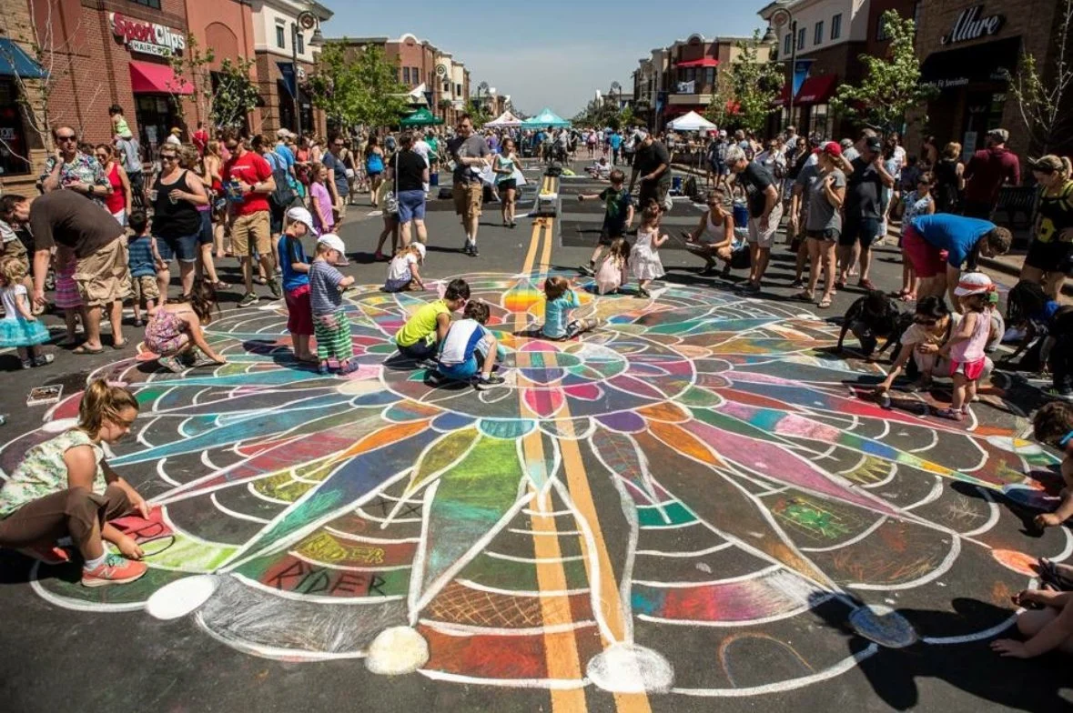 People creating a large colorful chalk art mural on a city street during a community event.