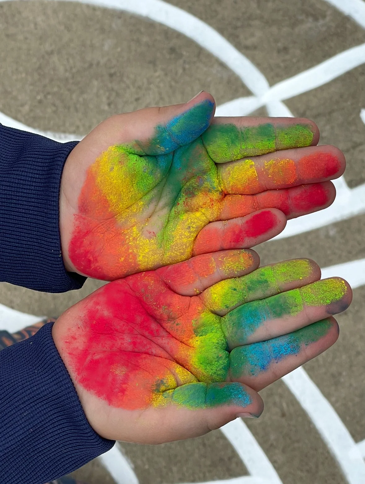 Two hands with colorful chalk paint in red, yellow, green, and blue, held over a basketball court with white lines.