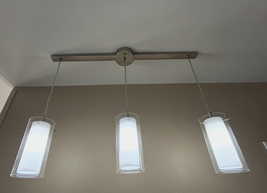 Ceiling-mounted light fixture with three cylindrical frosted glass lights hanging from a metal bar.