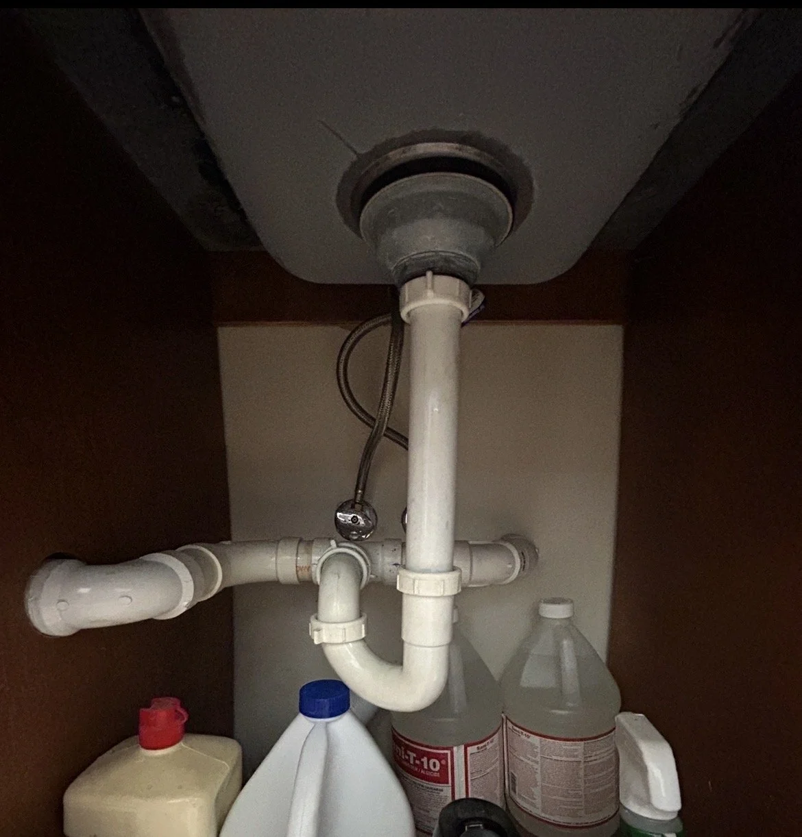 Pipes and plumbing under a kitchen sink with cleaning supplies stored beneath.