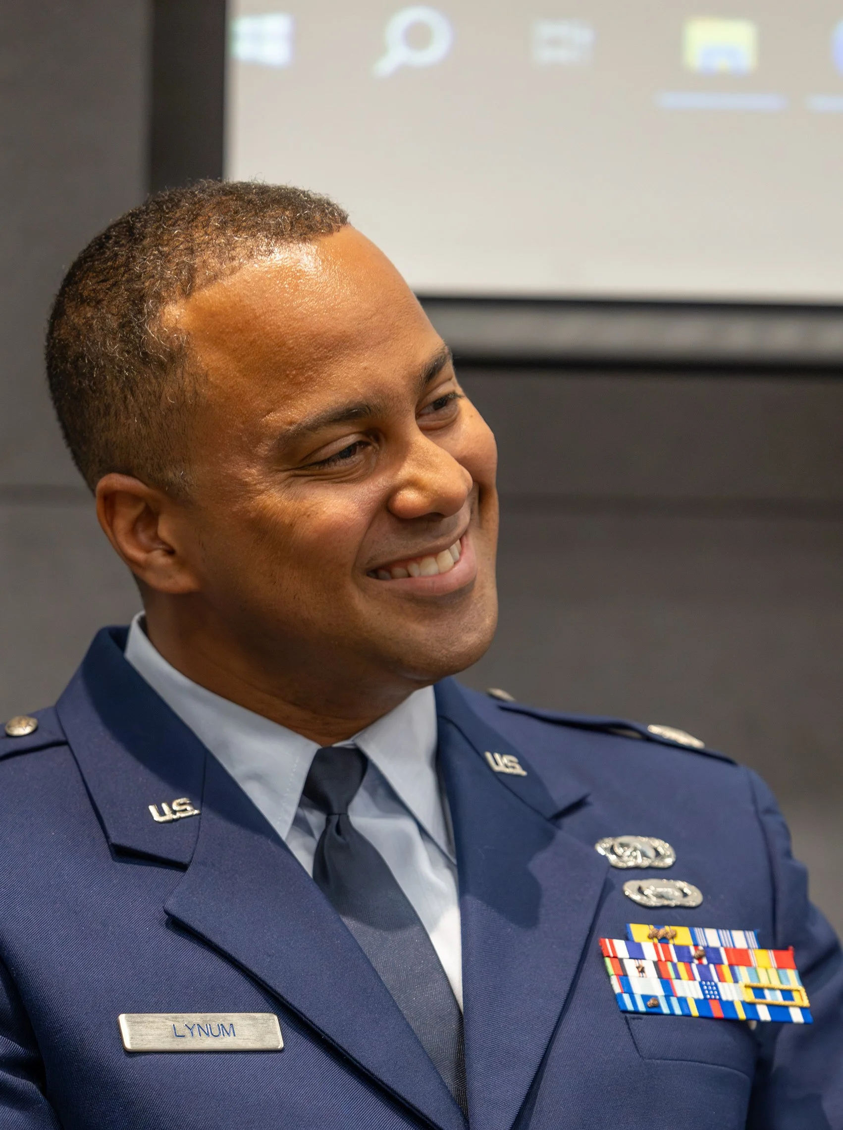A smiling man in a U.S. Air Force dress uniform with medals and a name tag that reads 'Lynum'.