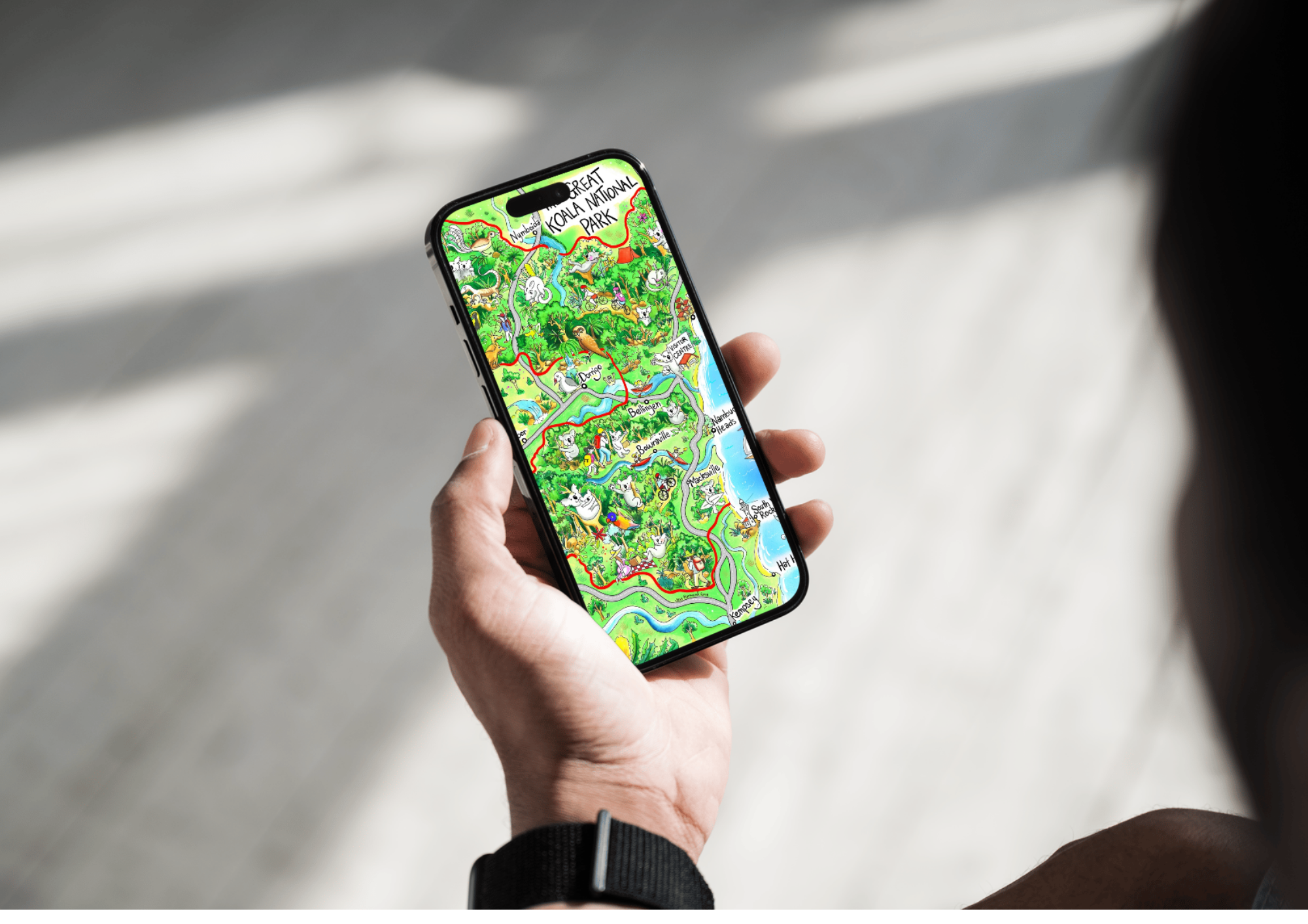 A person holding a smartphone displaying a colorful illustrated map of Koala Creek National Park with various animals and landmarks.