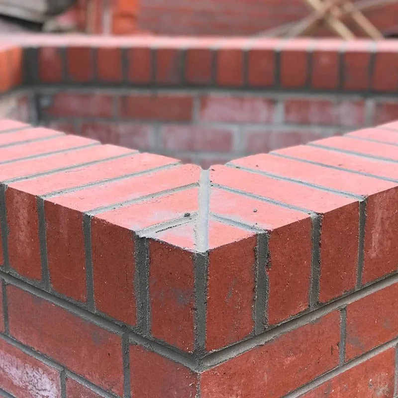 Close-up of a corner of a brick structure with red bricks and gray mortar, showing the neat brickwork.
