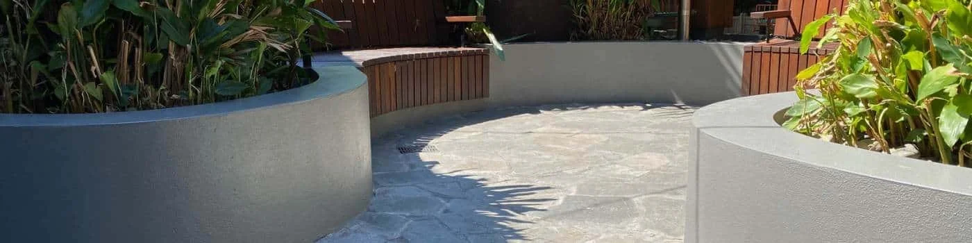 Outdoor curved concrete planters with green plants, wooden panel accents, and a stone pathway.