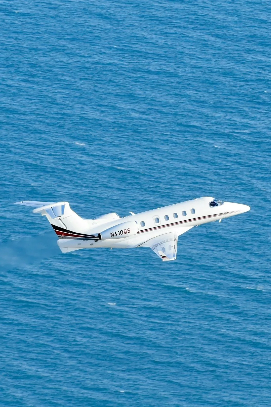 A white private jet flying over the ocean.