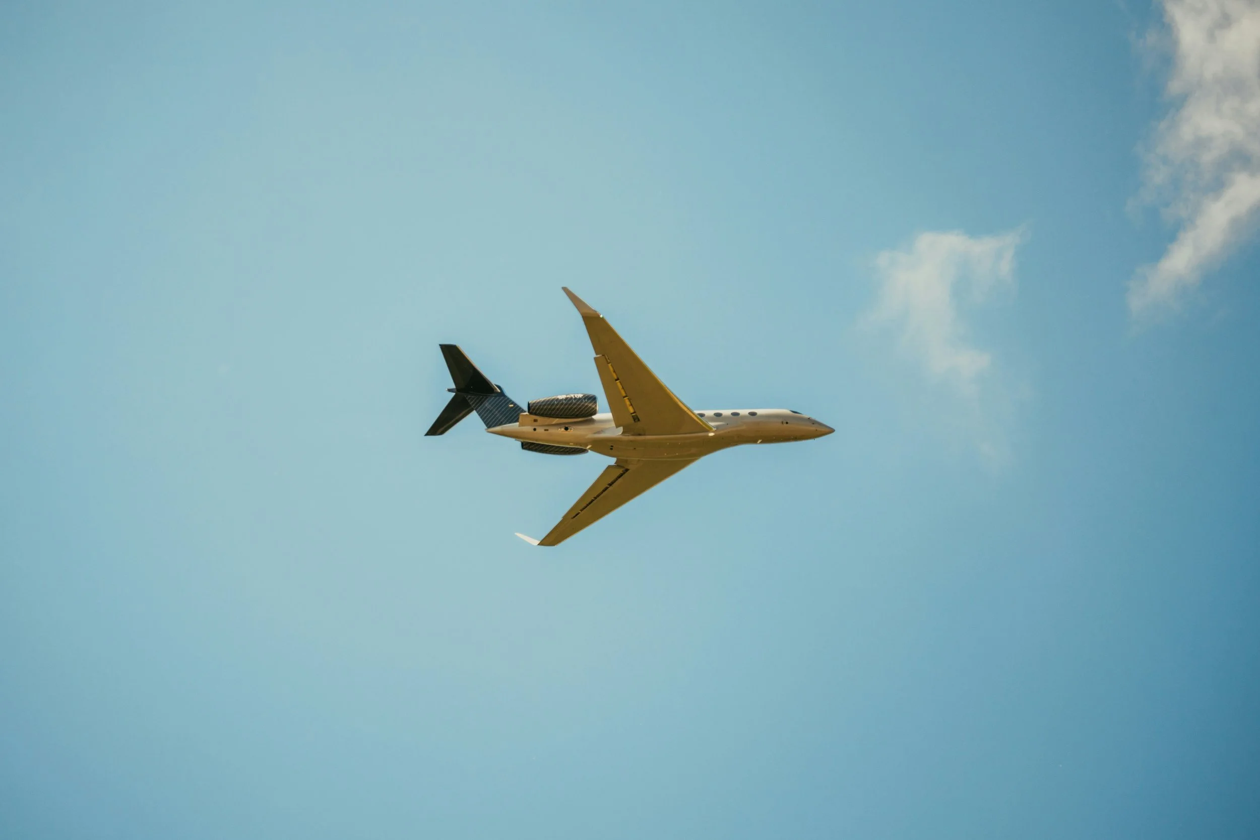 A private jet flying in a blue sky with a few clouds.