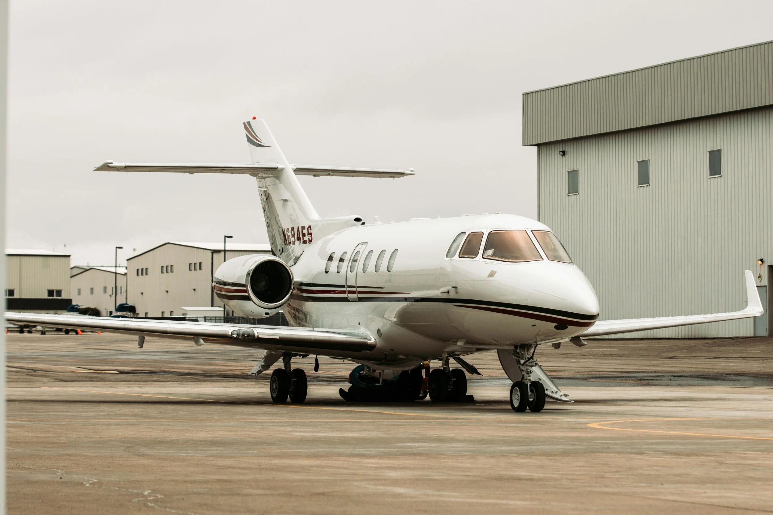 Private jet parked on the tarmac near hangar buildings with overcast sky.