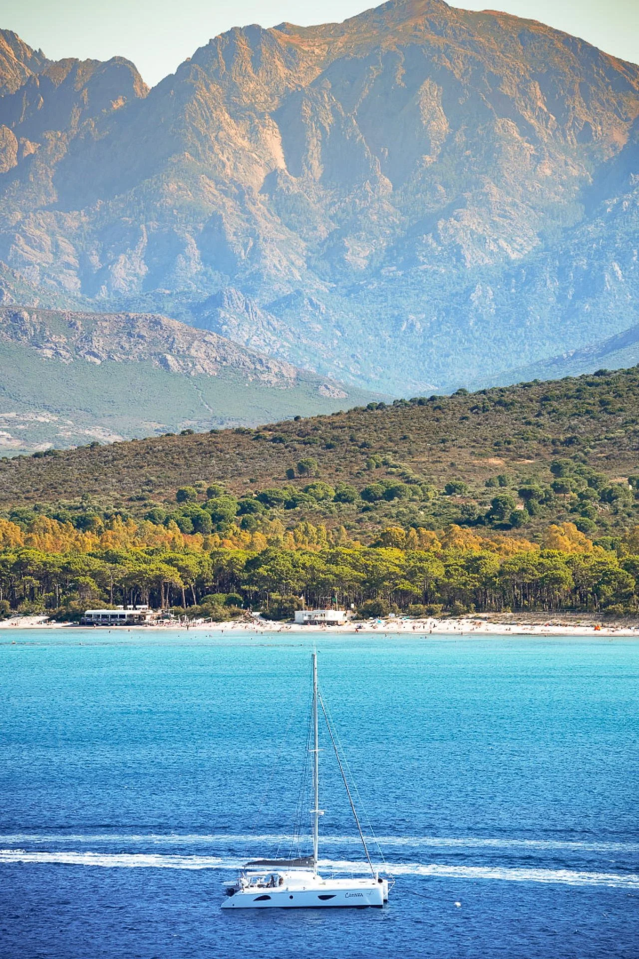 A sailboat on a lake with mountains in the background and a forested shoreline.