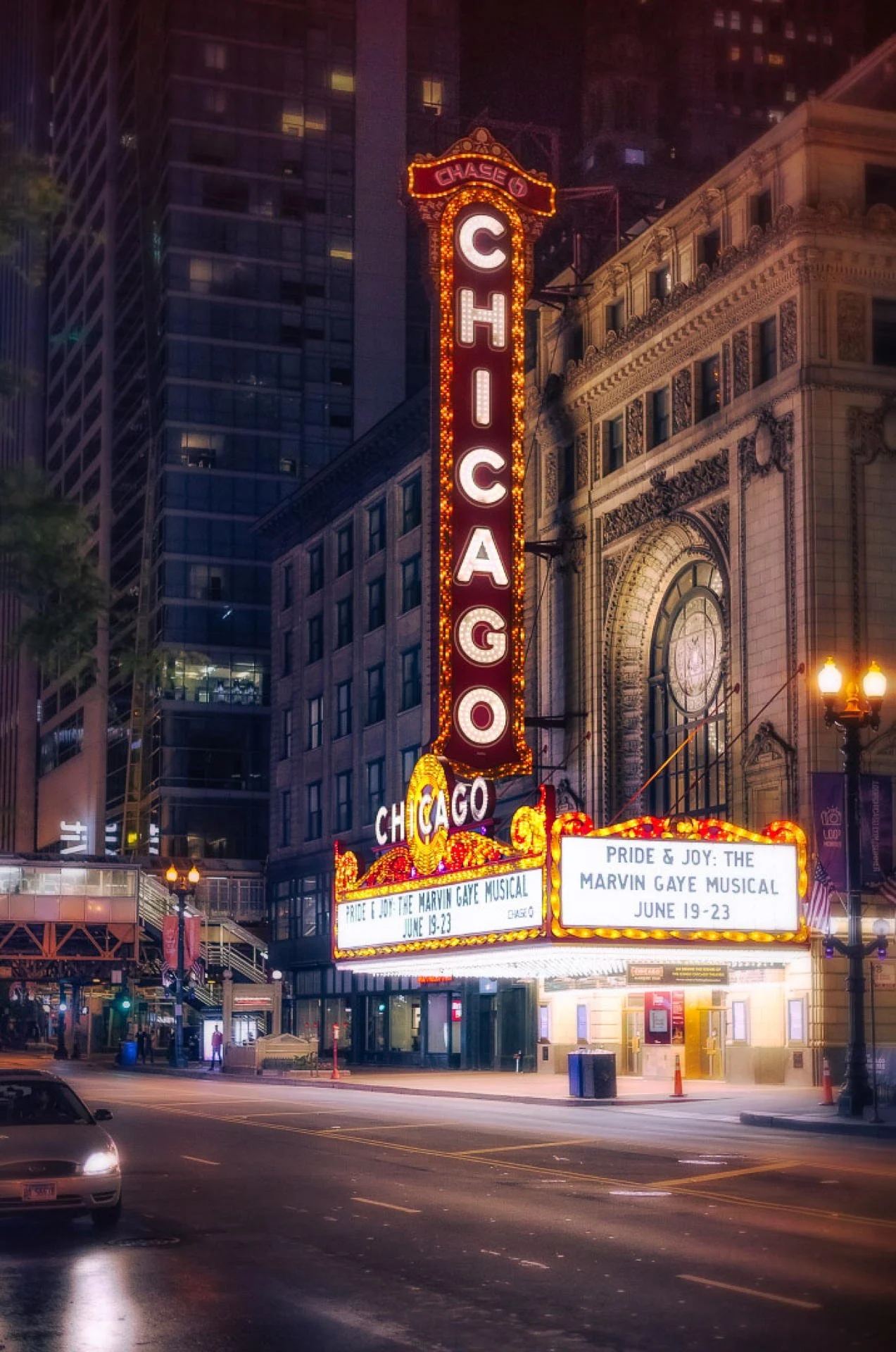 Night view of the Chicago Theater marquee sign with bright lights, announcing the musical 'Pride & Joy: The Marvin Gaye Musical' happening June 19-23, surrounded by tall buildings and city lights.
