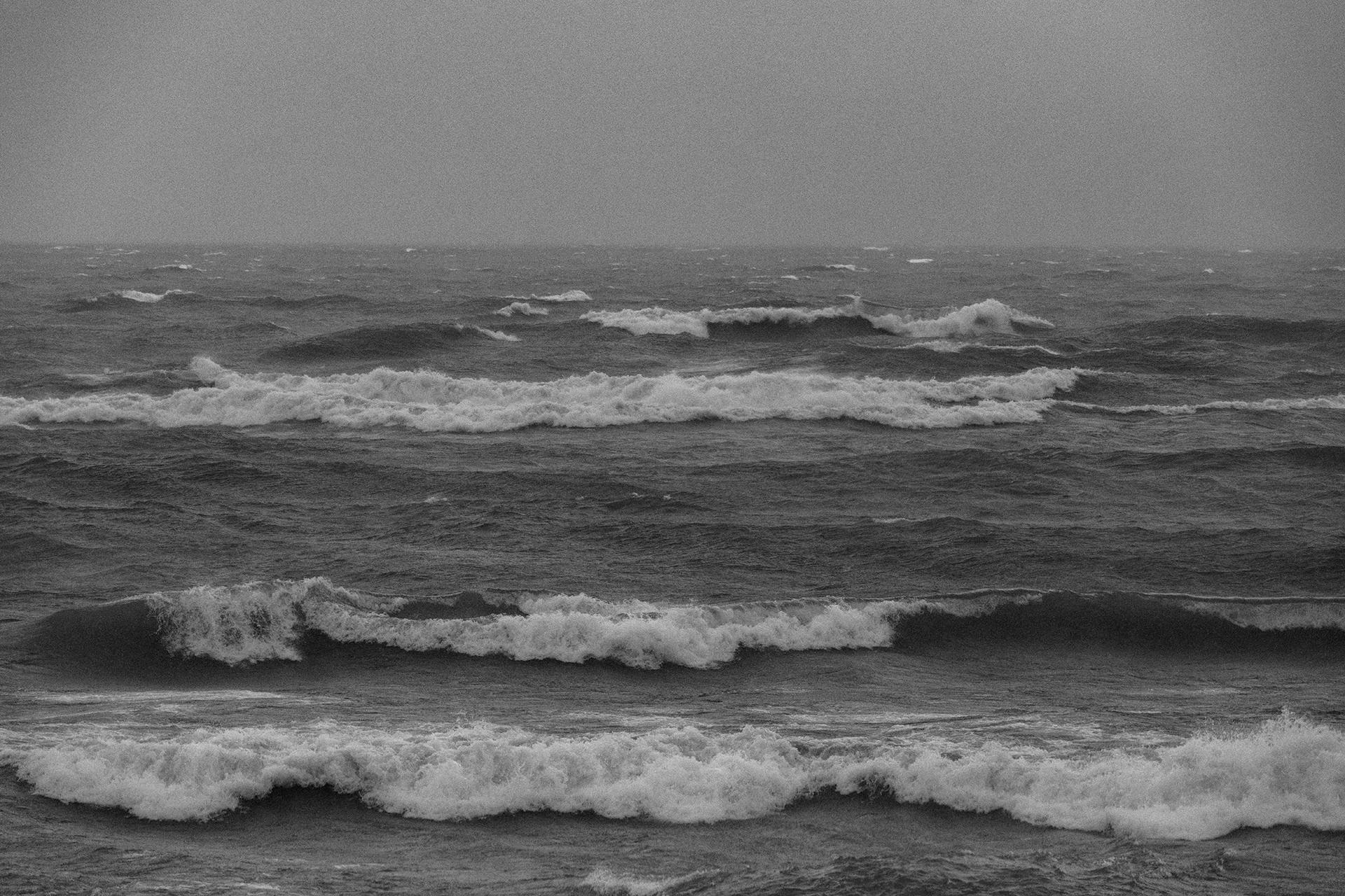 Black and white photo of ocean waves with a cloudy sky.