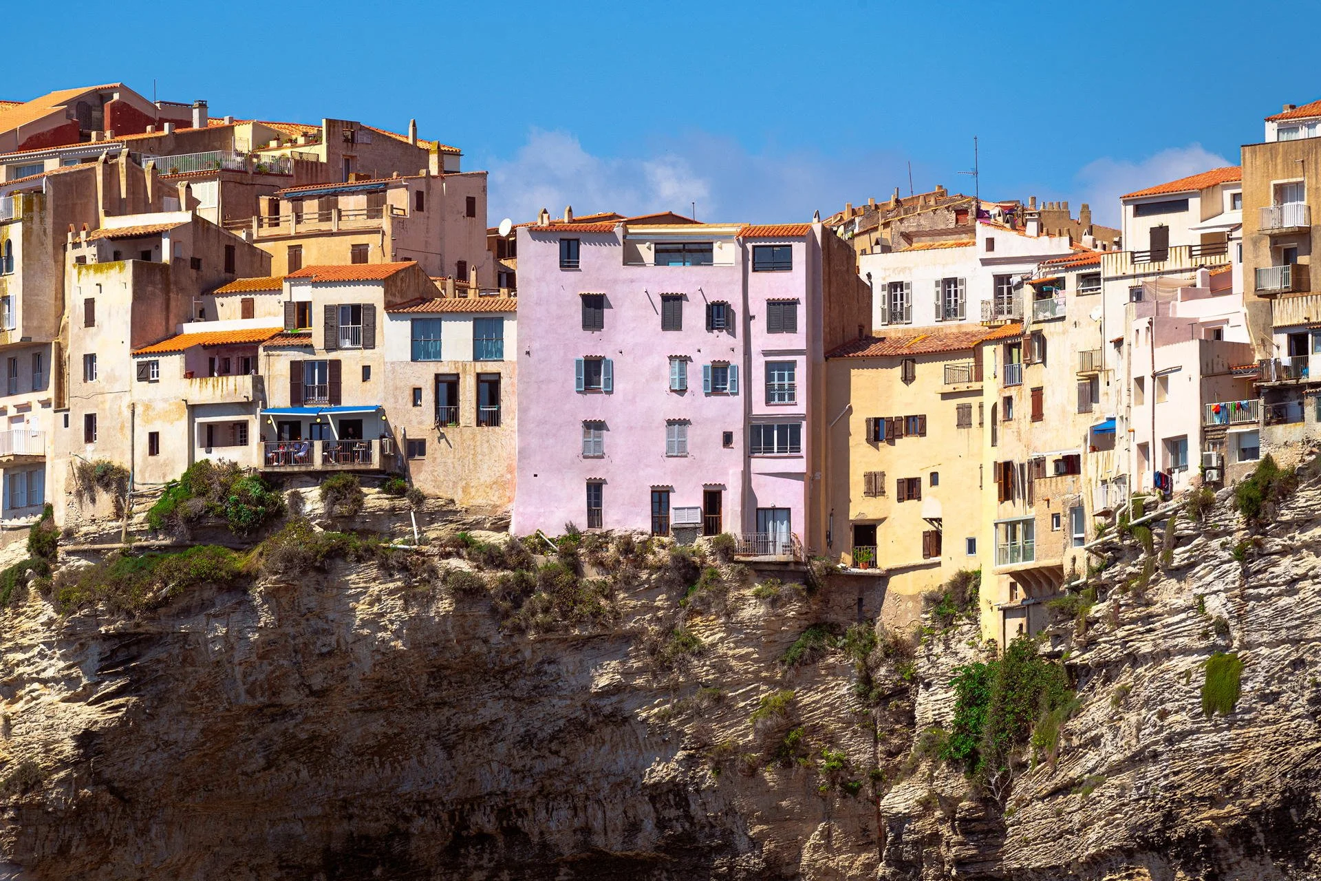 Colorful multi-story buildings on a rocky cliff under a blue sky.