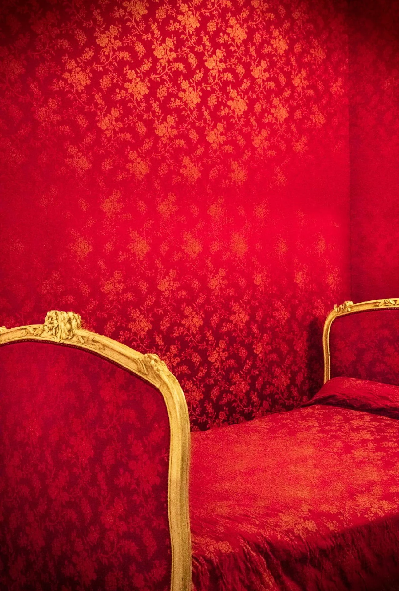 Luxurious red bedroom with patterned red wallpaper, gold-trimmed headboard, and matching bedspread.