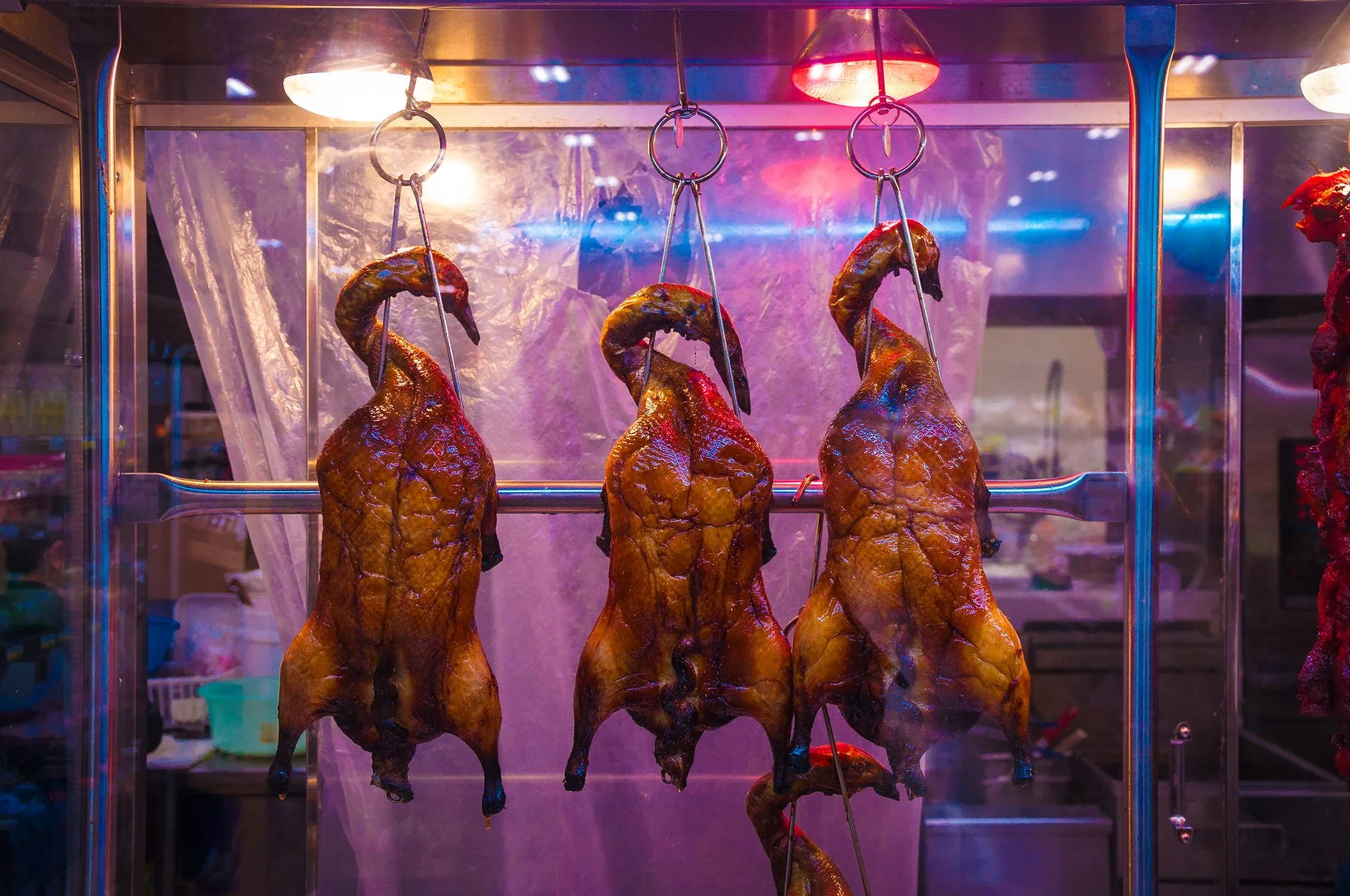 Three roasted ducks hanging inside a glass display case