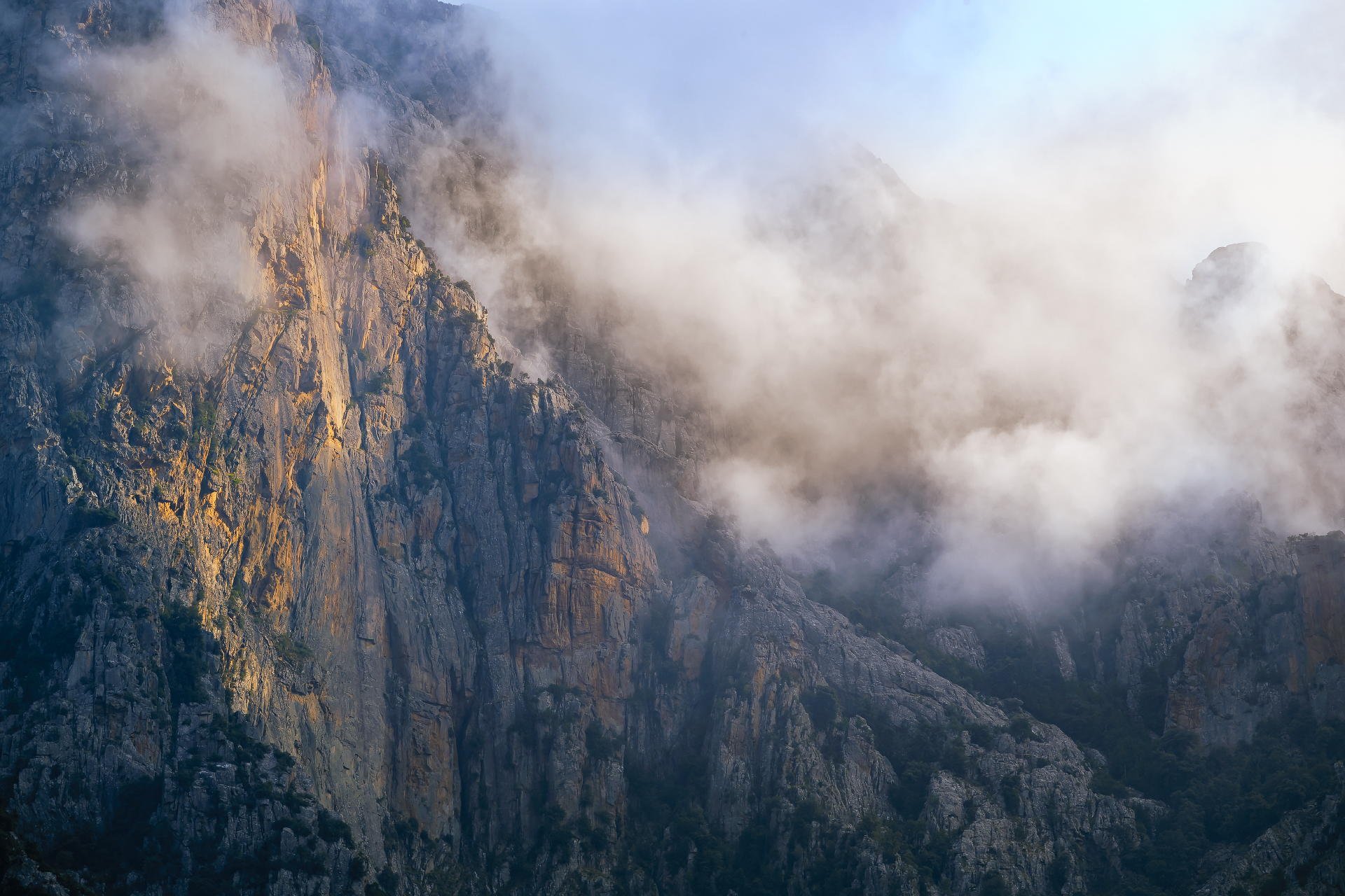 A mountain with rocky cliffs partially covered in mist or low clouds