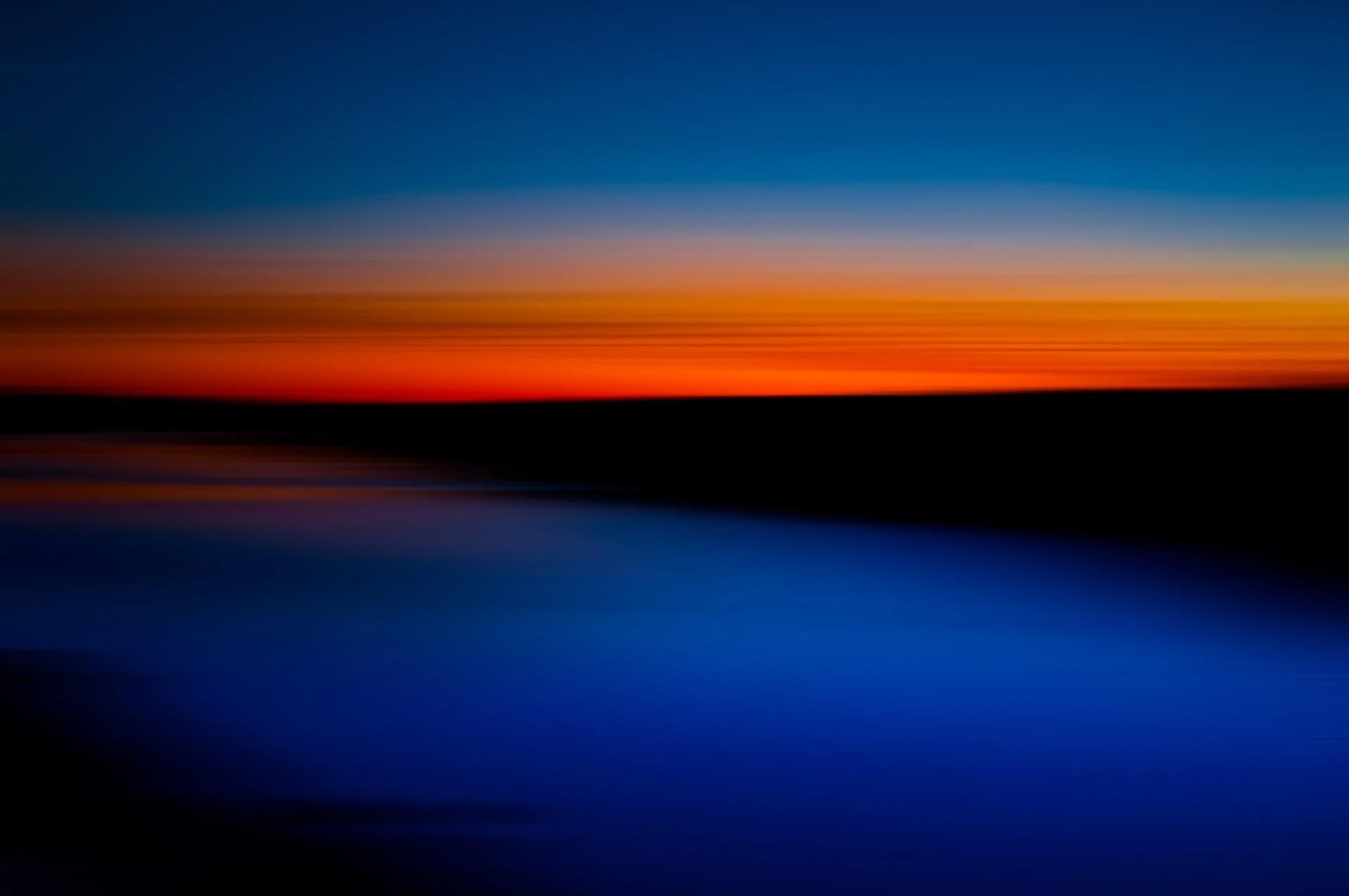 Blurred sunset over water with horizontal bands of orange, red, blue, and black colors.