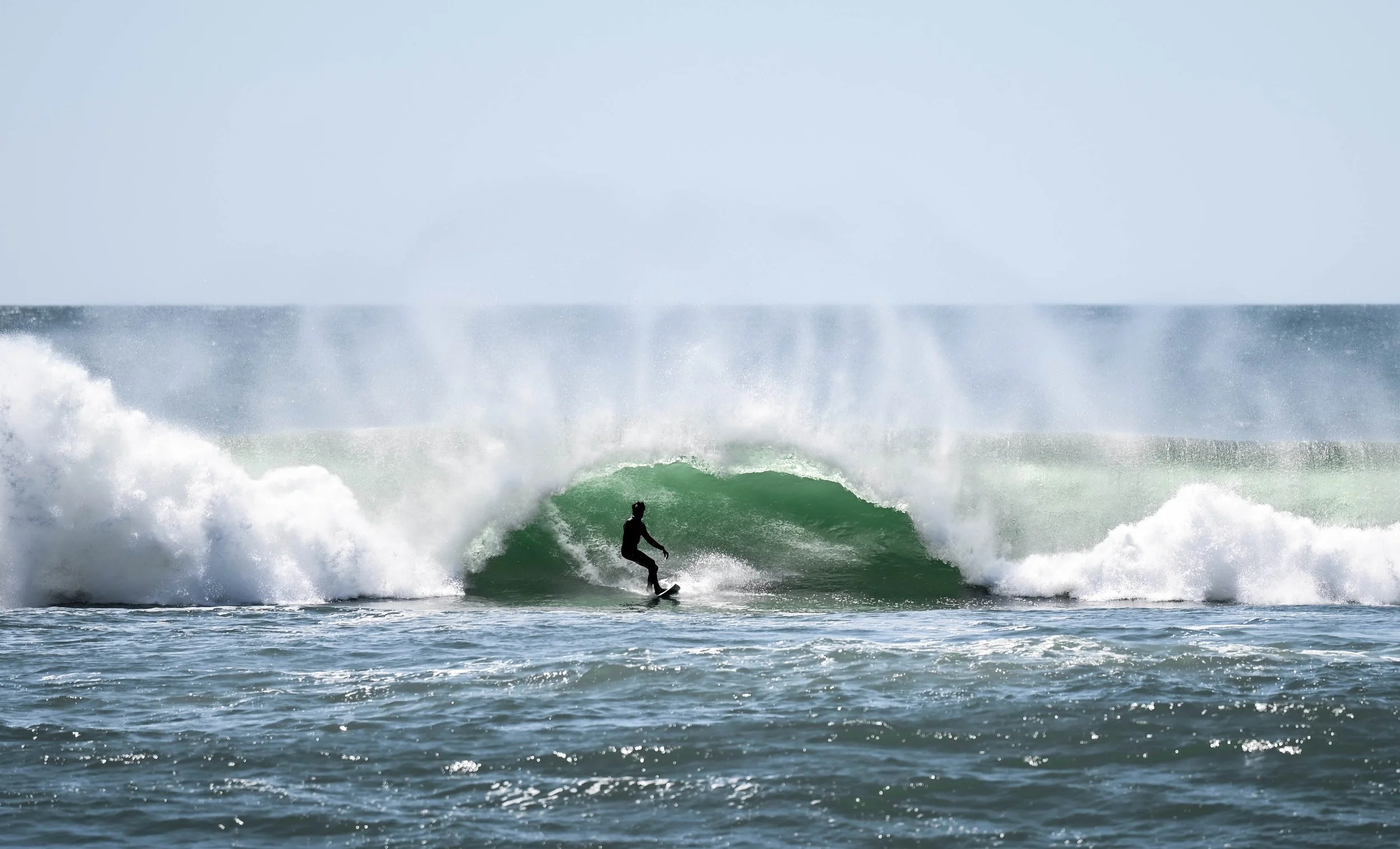 Silhouette of a person surfing on a wave in the ocean with the sky in the background.