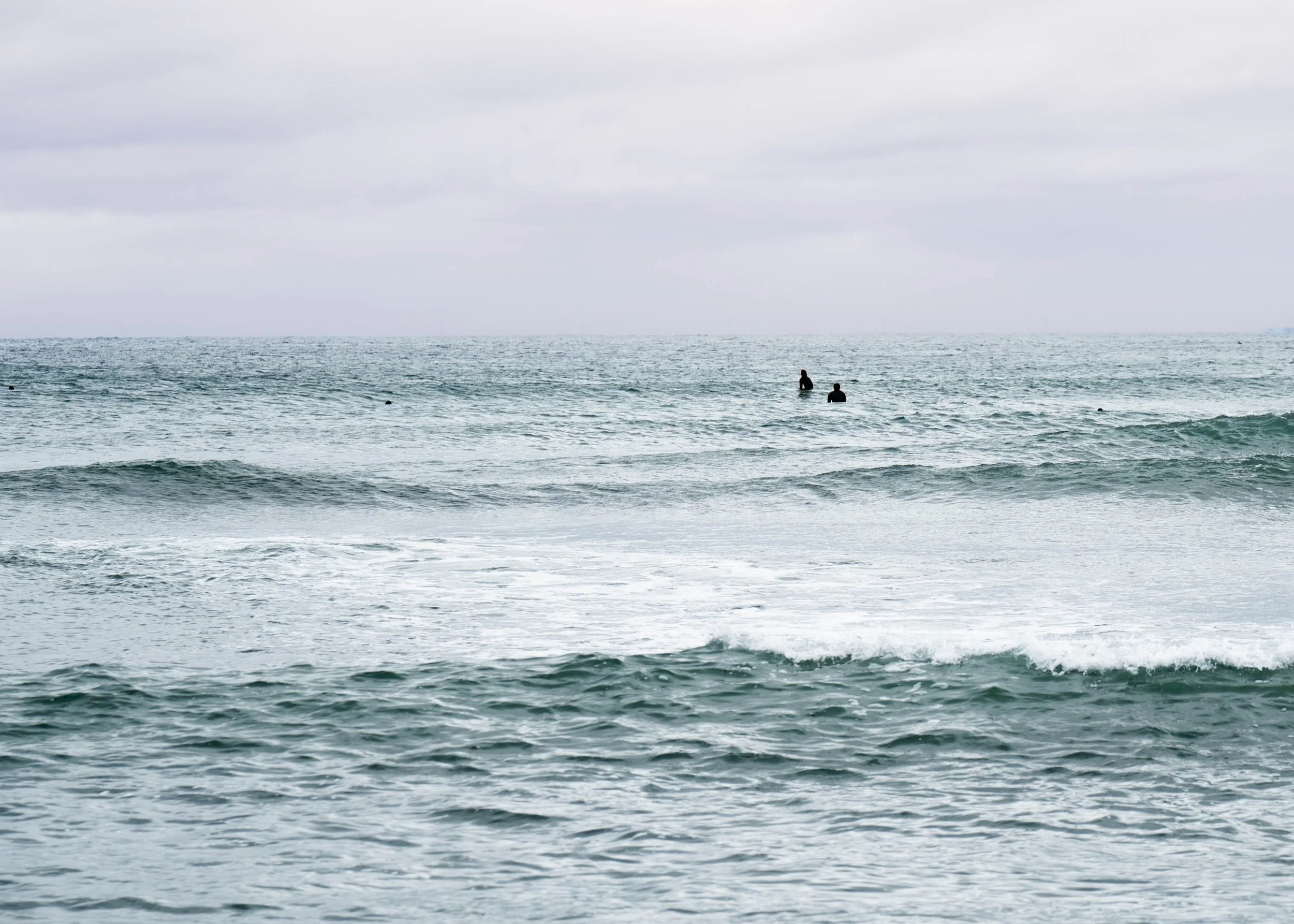Two people sitting or standing in the ocean with cloudy sky above.