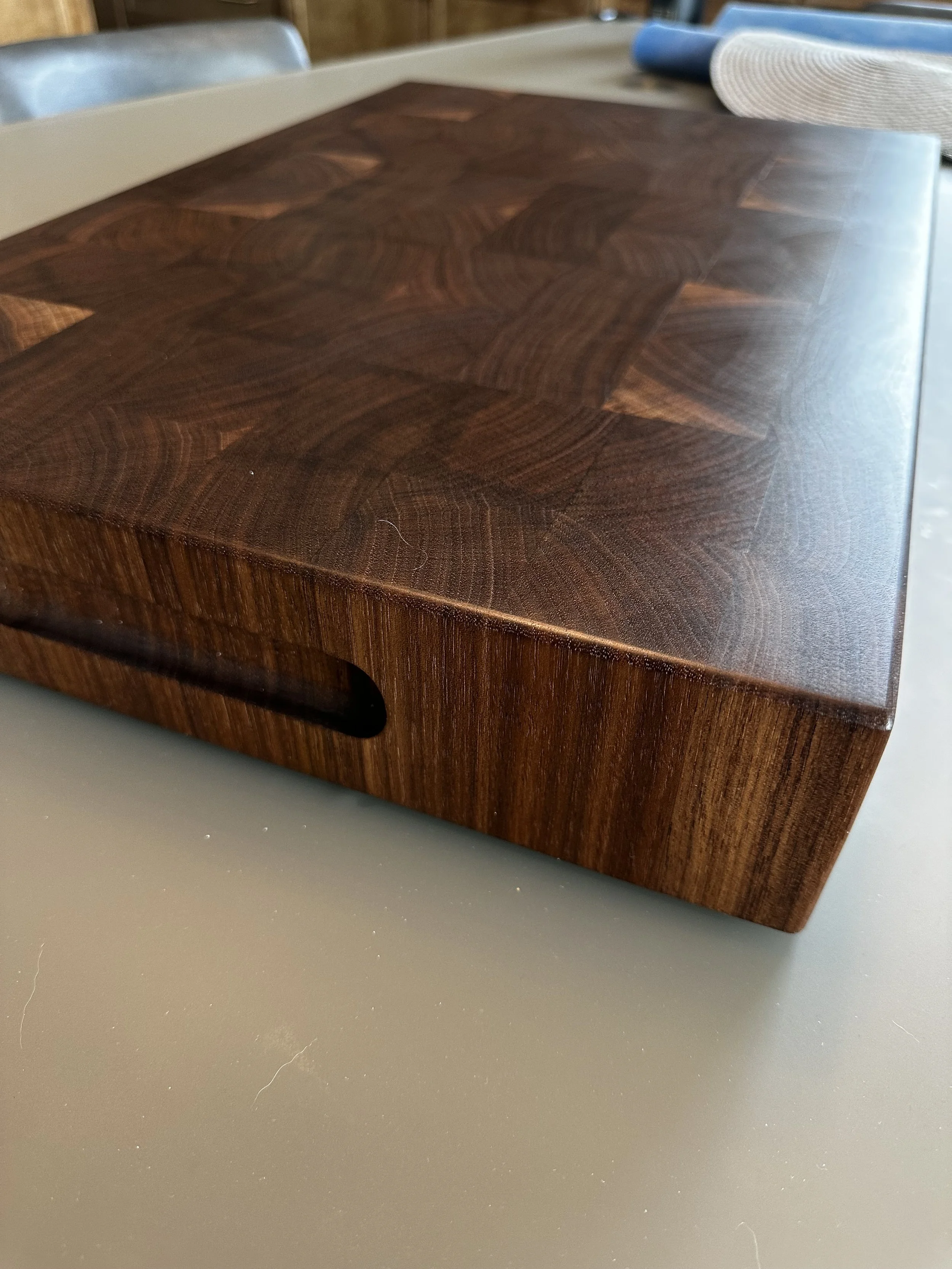 Close-up of a wooden cutting board with a handle on a gray table.