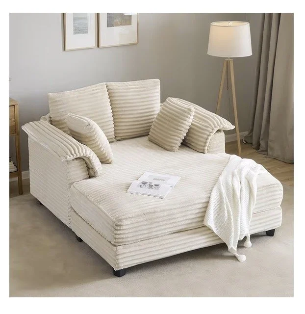 A white striped hammock-style couch with pillows, a white knit blanket, and a magazine on it, in a cozy living room with a floor lamp, framed pictures, and curtains.