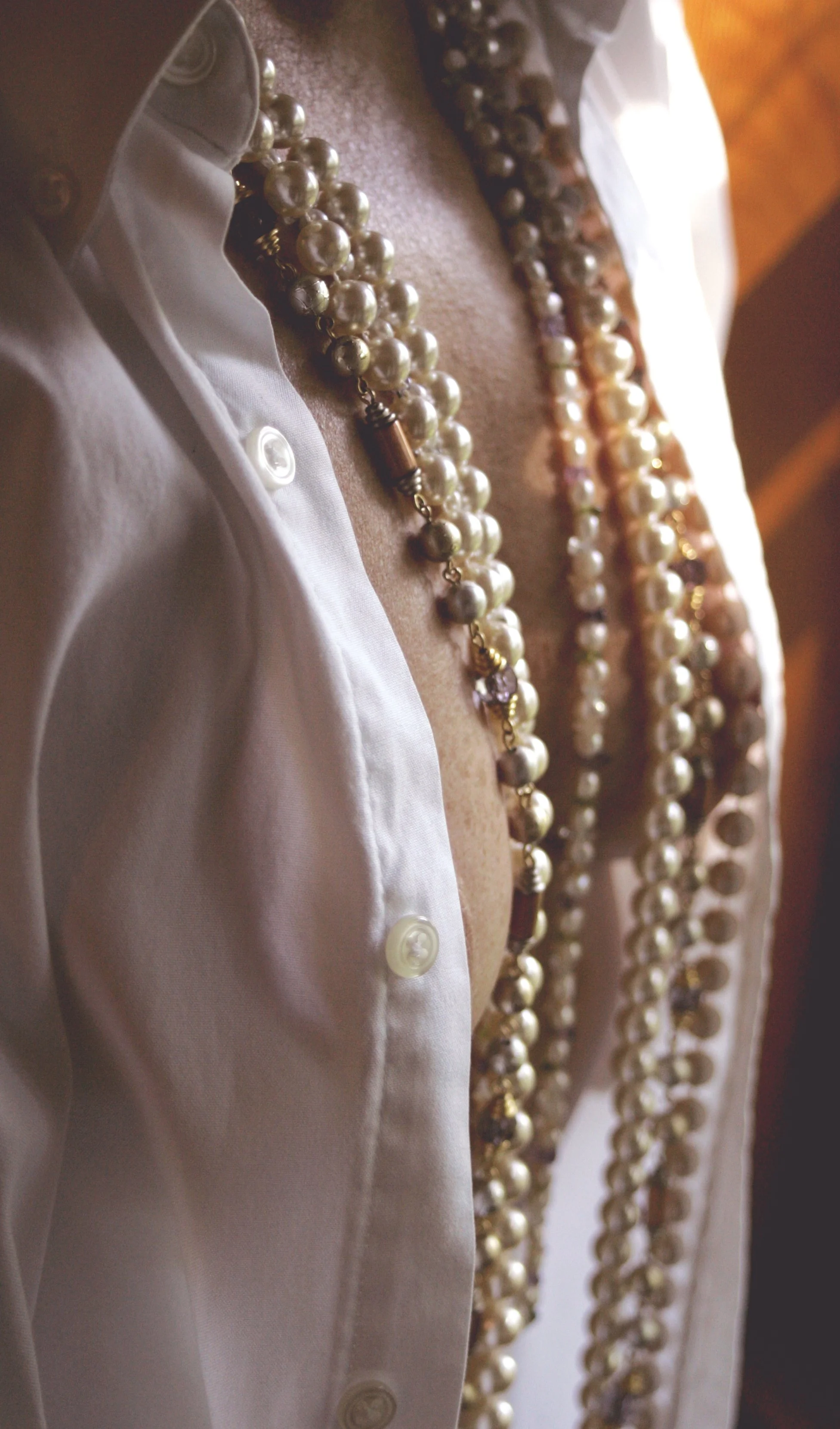 Close-up of a person wearing a white shirt slightly unbuttoned, with multiple pearl necklaces around their neck.