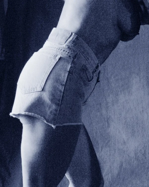 Close-up of a person wearing denim shorts and a dark top, standing with one leg slightly bent.