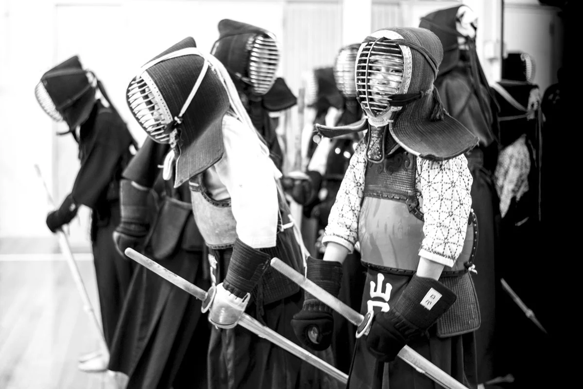 Group of children dressed in kendo armor, practicing kendo with shinai swords in a dojo.