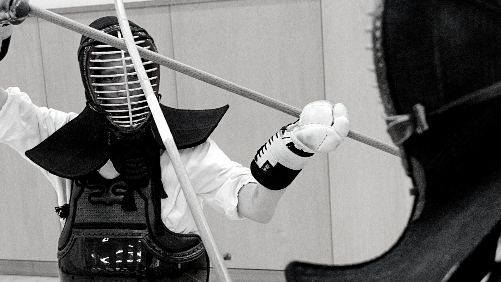 Two naginataka in protective gear engaging in a naginata match, both wearing masks and gloves.