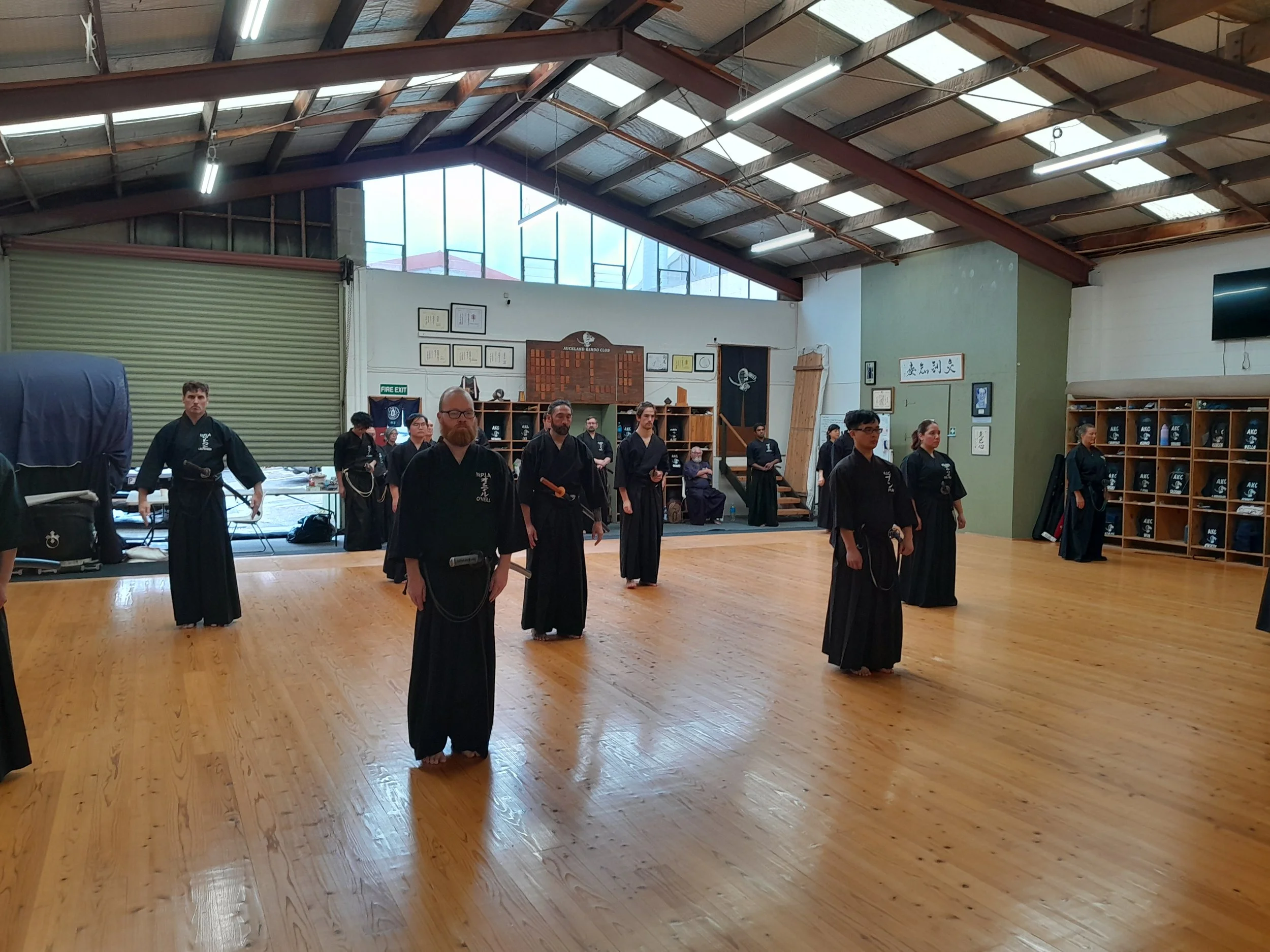 People practicing martial arts in traditional uniforms in indoor gym with wooden flooring and high ceiling.