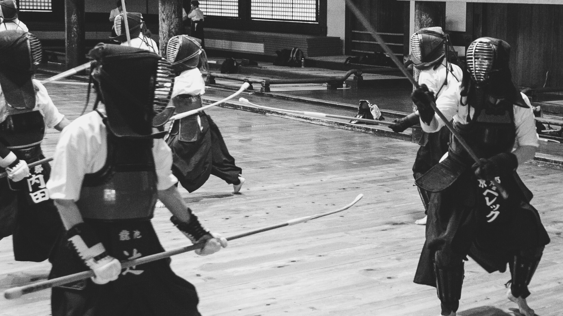 Group of martial artists practicing naginata in a gym, wearing protective gear. Historical photo.