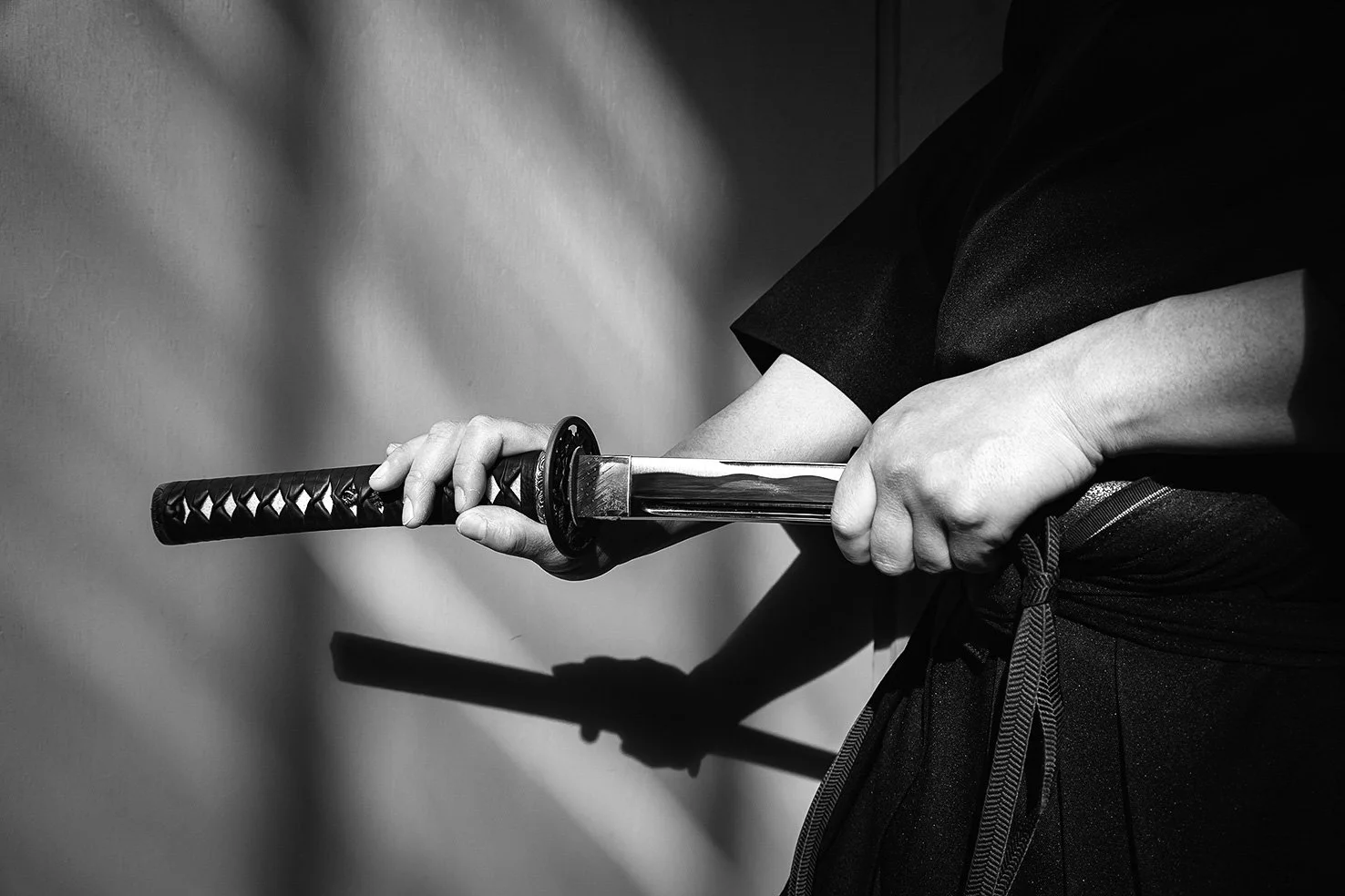 Person holding a katana sword in a defensive stance, dressed in black martial arts attire.