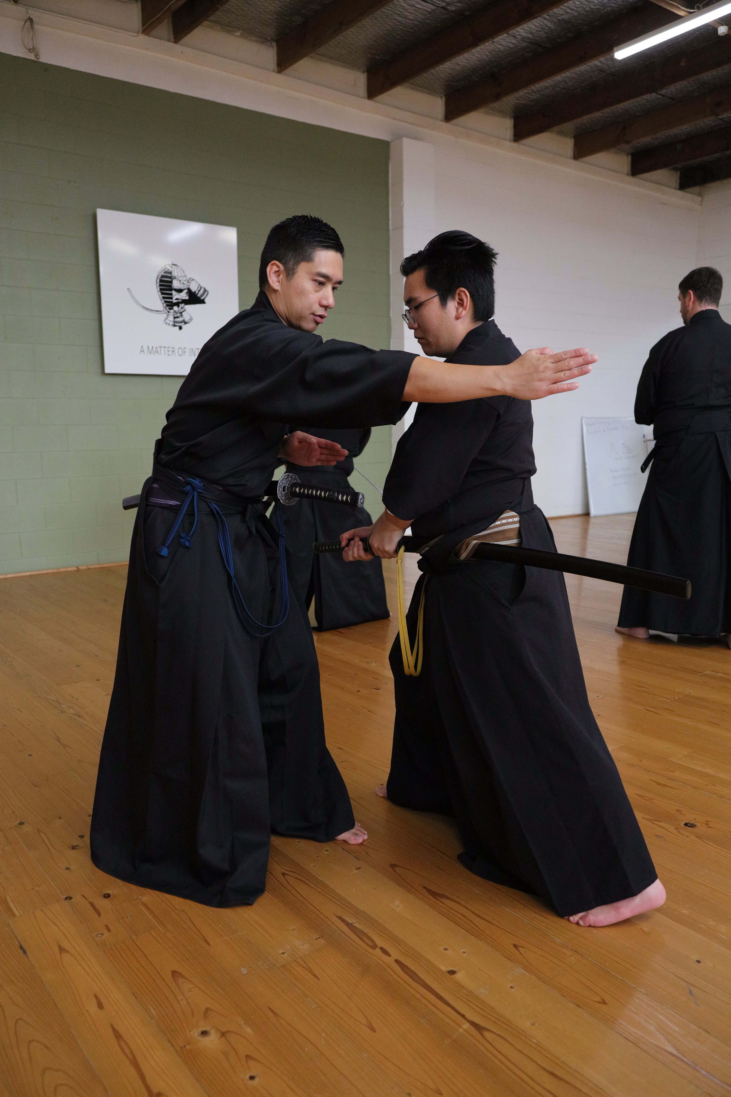 Two men practicing martial arts, with one performing a strike or block on the other during a training session in a dojo.