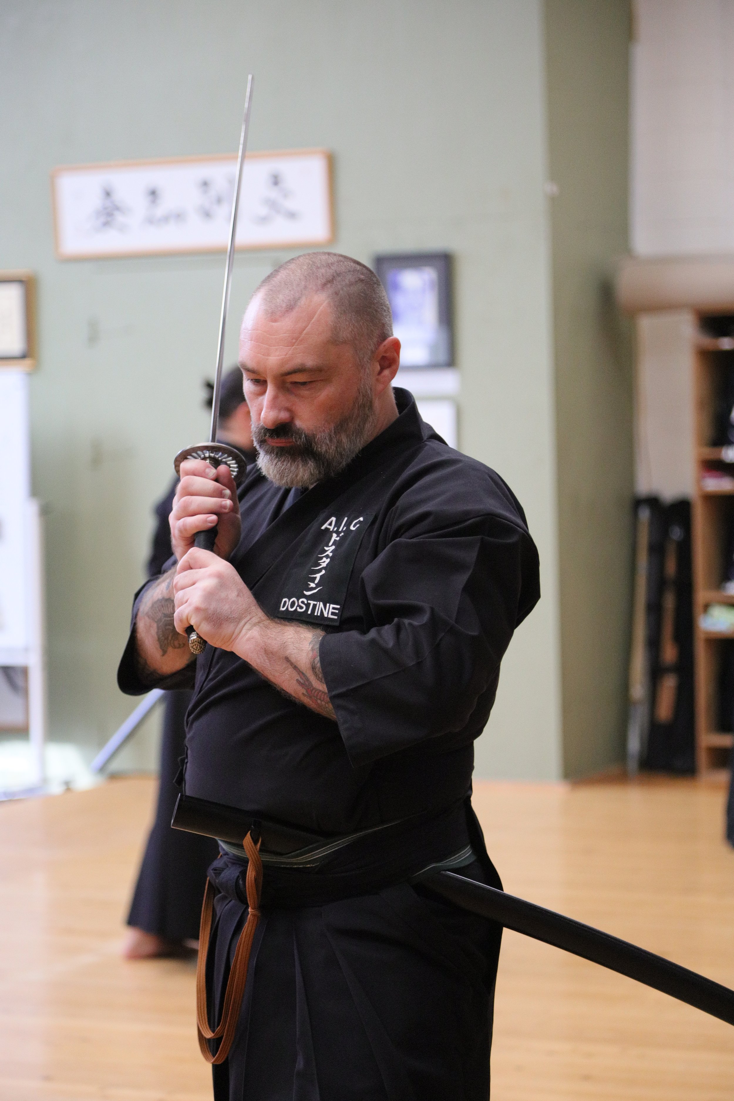 A man in a black martial arts uniform practicing Kendo with a shinai sword in a dojo.