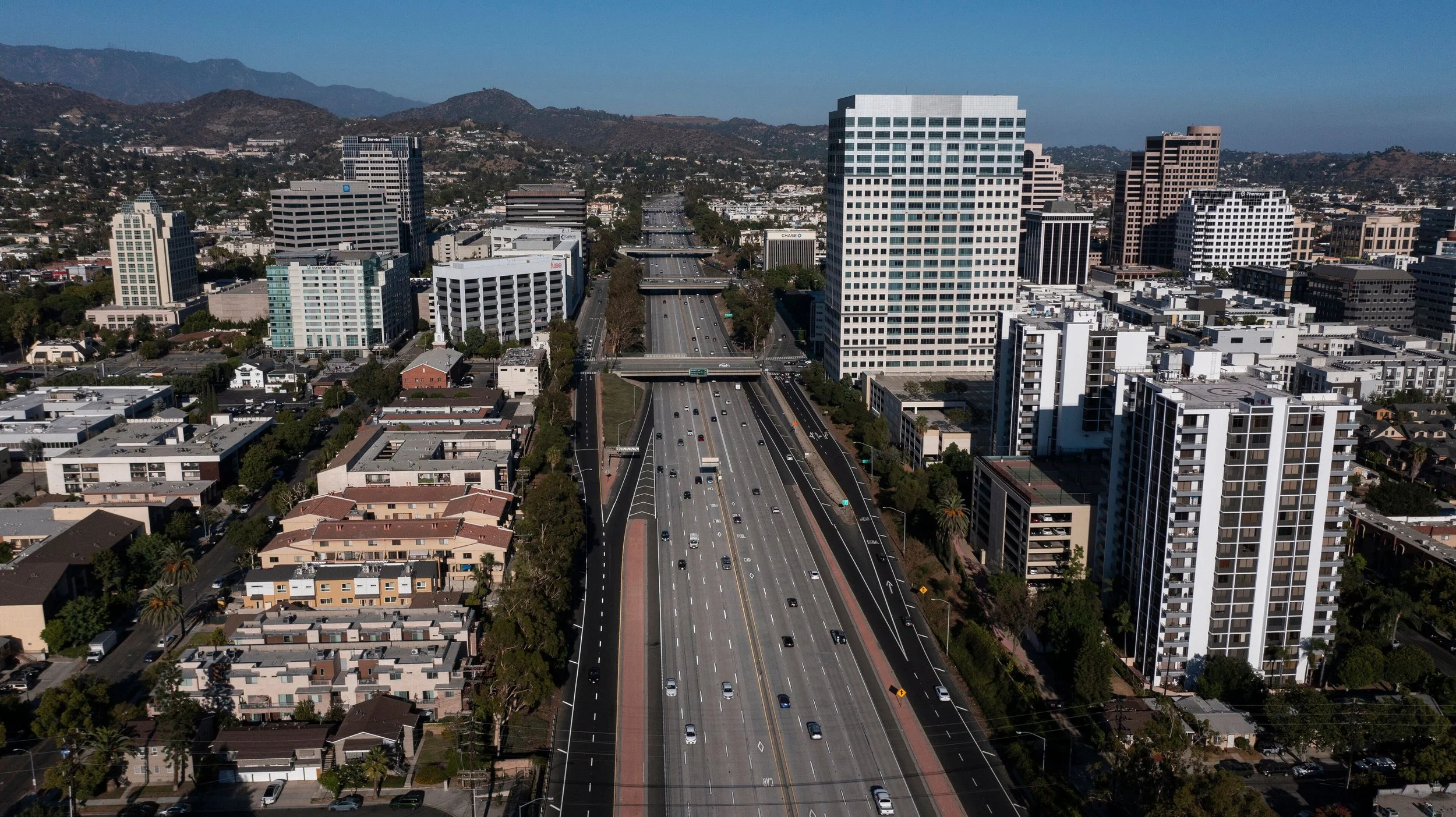 Aerial view of a city of Glendale, CA with tall skyscrapers, roads, and mountains in the background.