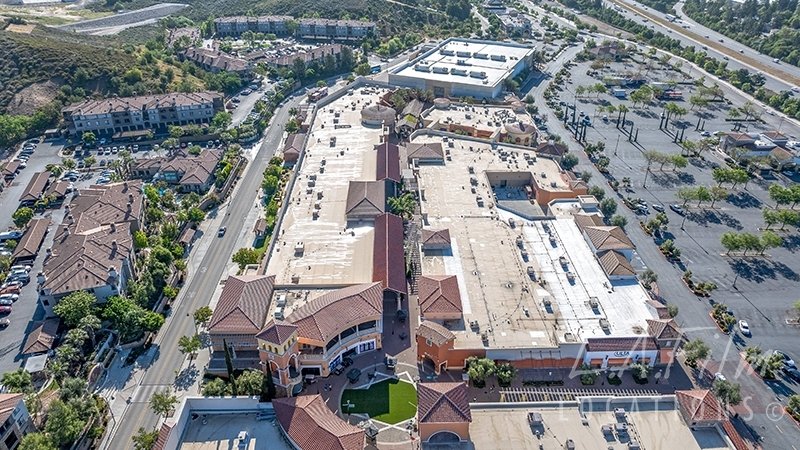 Aerial view of a Simi Valley, CA large shopping mall with a parking lot , surrounded by trees and residential buildings.