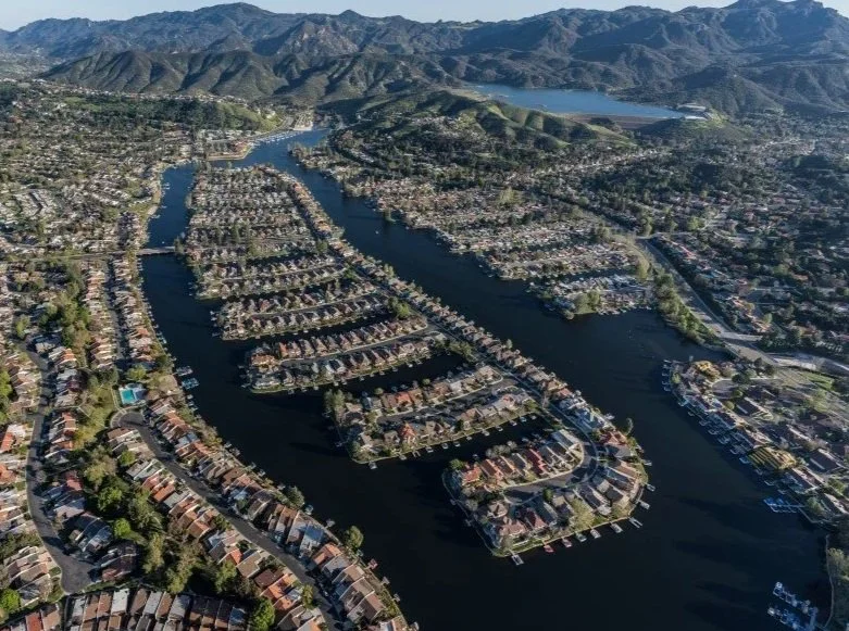 Westlake Village aerial view of a residential neighborhood with houses on a waterway, surrounded by mountains in the background.