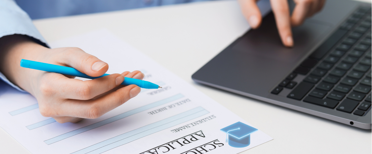 A person holding a blue pen over a scholarship application form on a desk, with a laptop nearby.