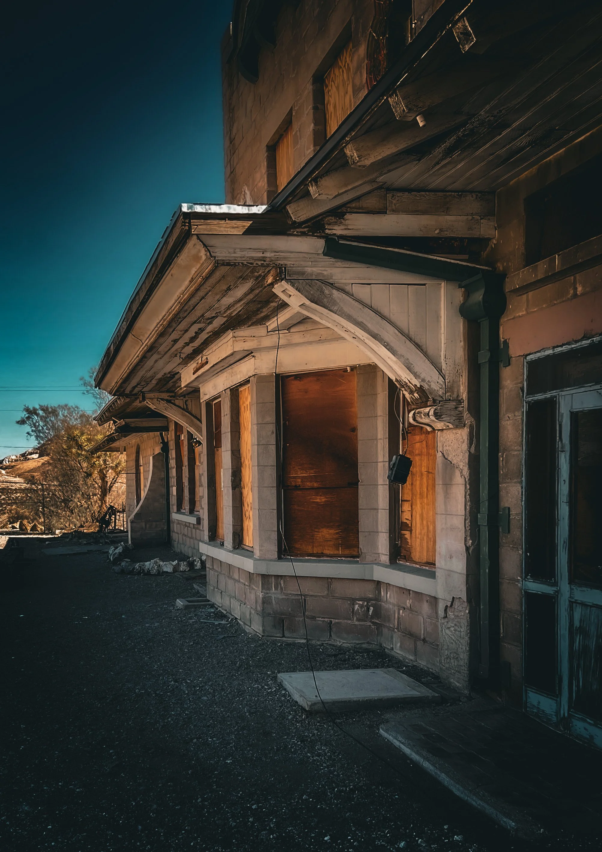 Abandoned building with boarded-up windows, cracked walls, and broken door, under a dark blue sky.